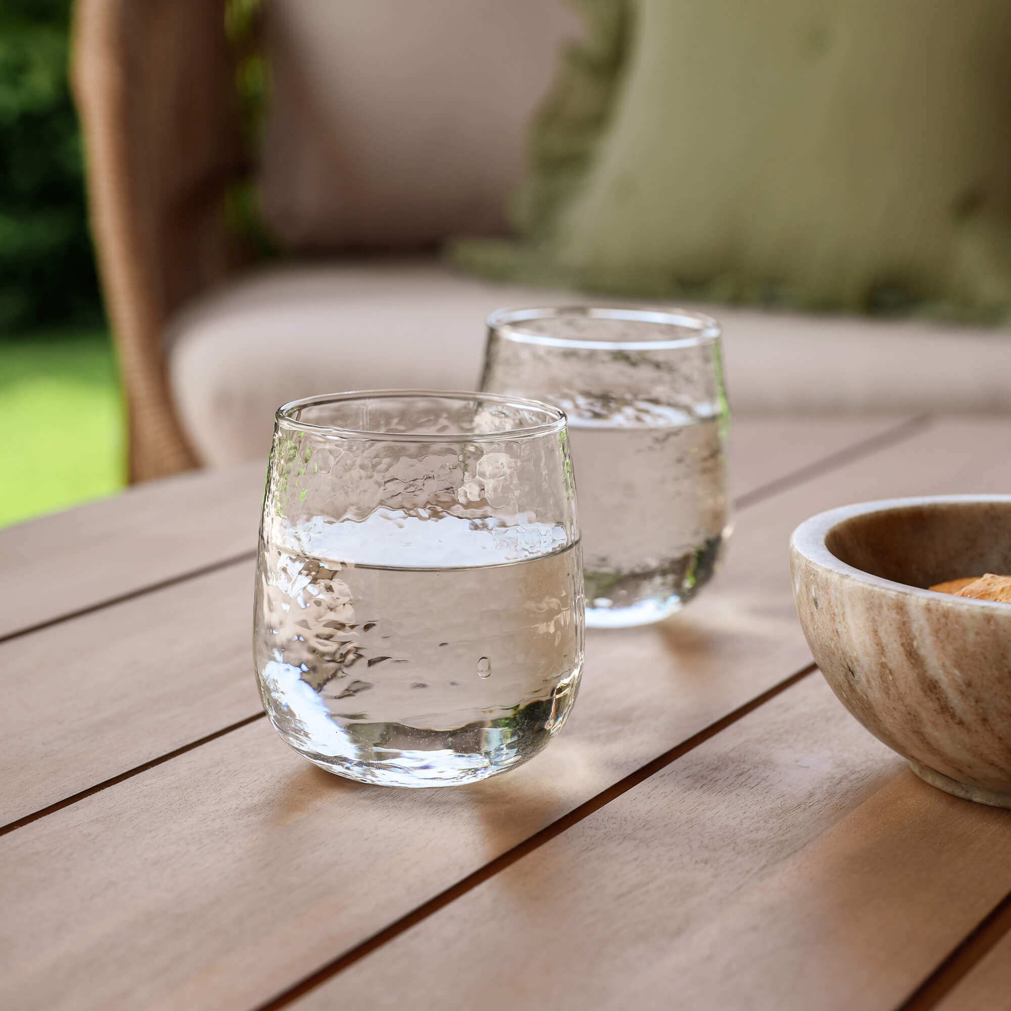 Twee doorzichtige glazen water op een houten tafel in de tuin naast een stenen kom