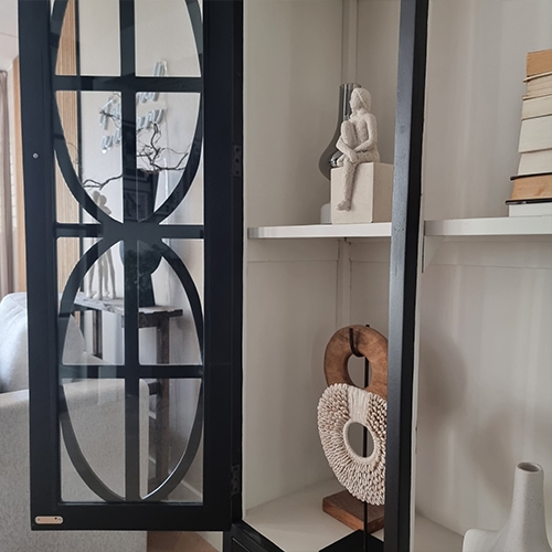 Zwarte metalen vitrine met decoratieve planken en sculpturen in lichte woonkamer