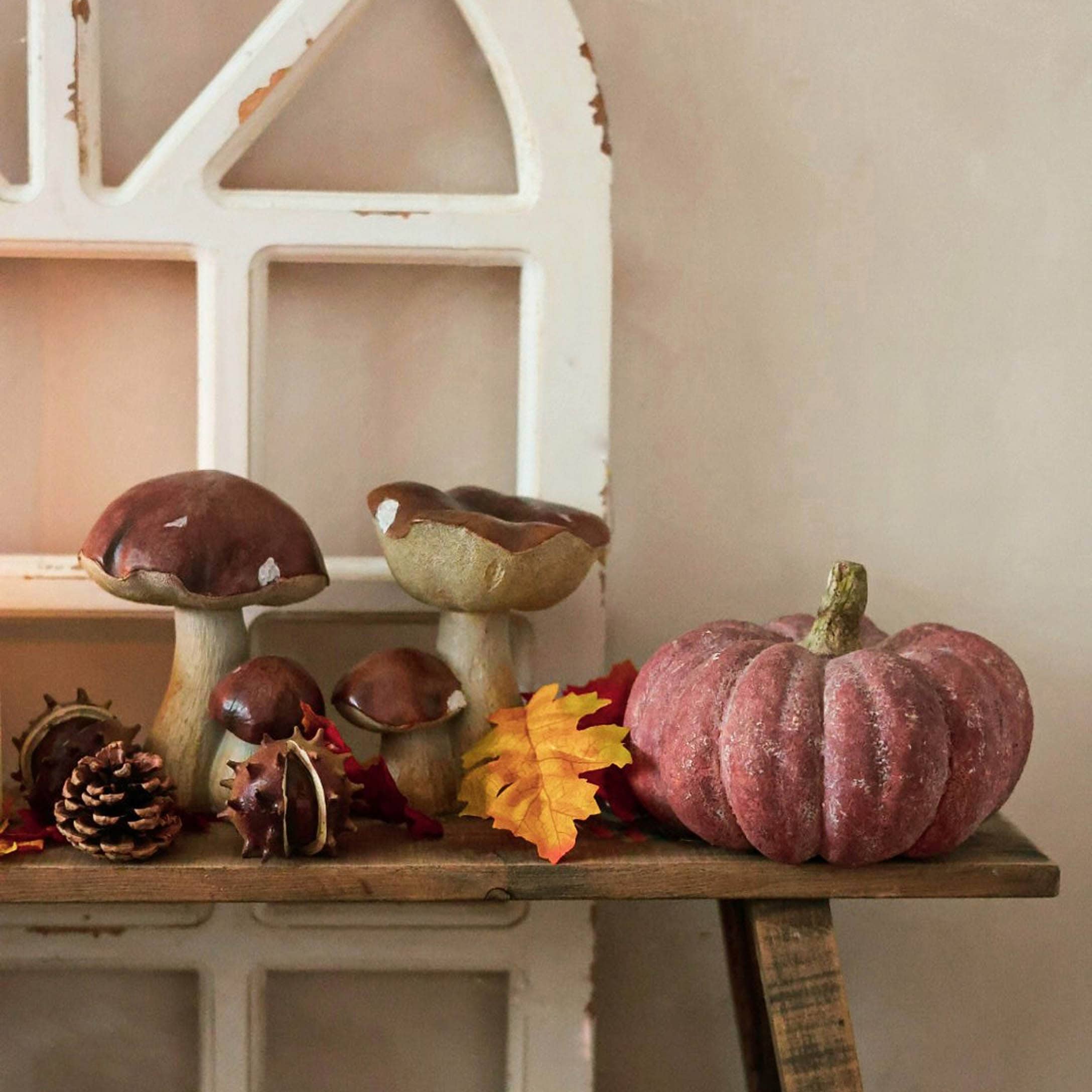 Herfstdecoratie met keramische paddenstoelen en roze pompoen op rustiek houten plank