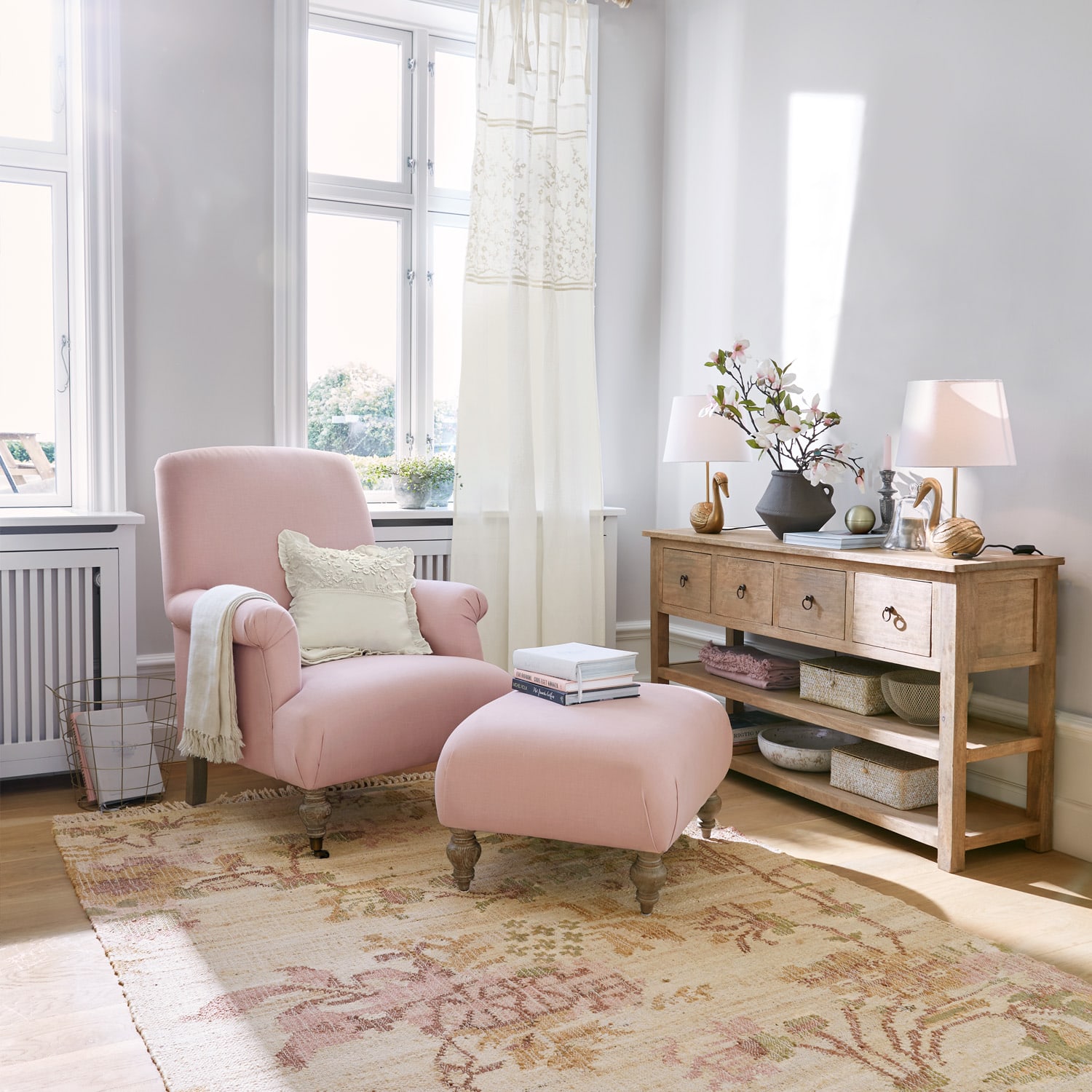 Roze stoffen fauteuil en voetenbank in lichte woonkamer met houten console en decoraties
