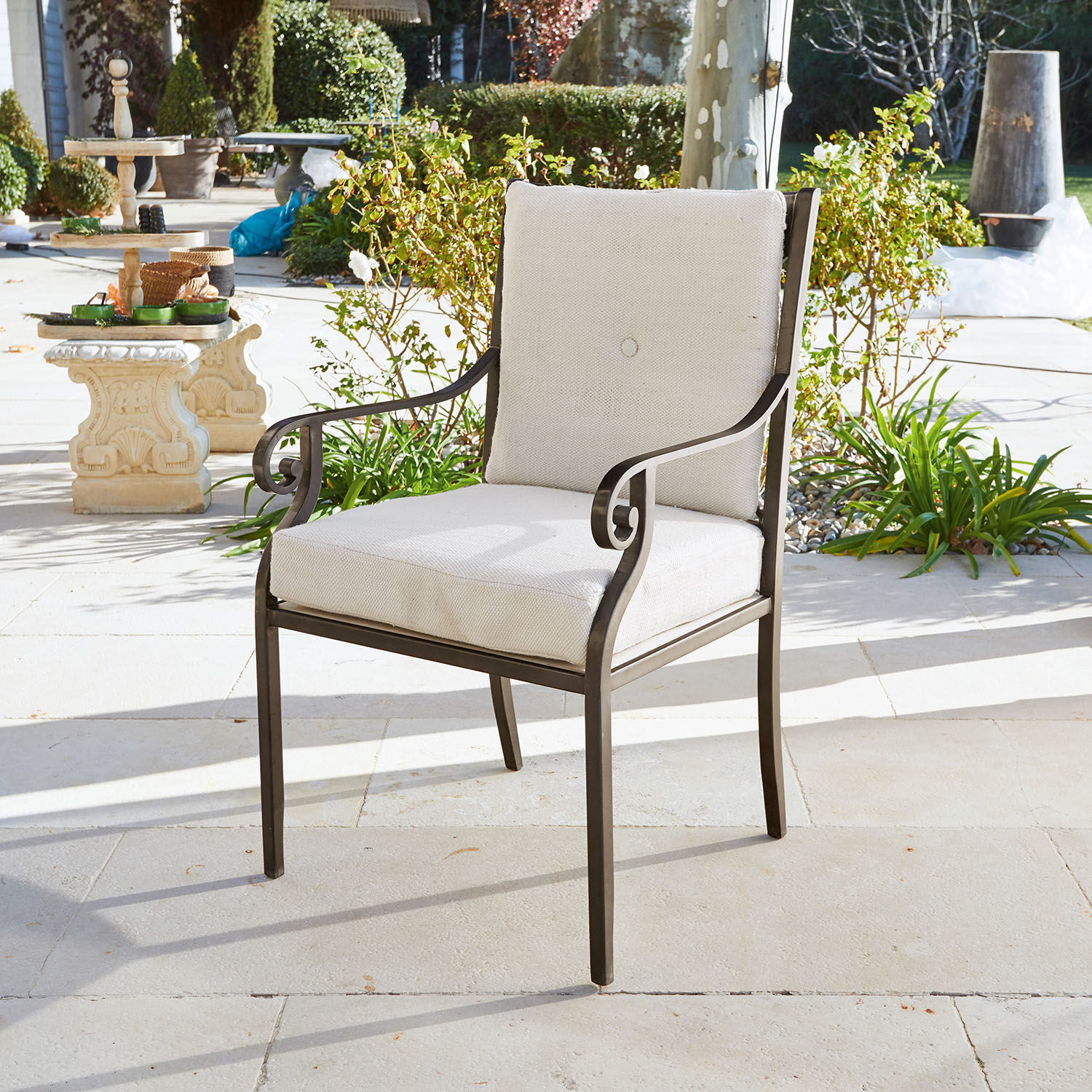 Tuinstoel met metalen frame en crèmekussen op lichte stenen terrasvloer