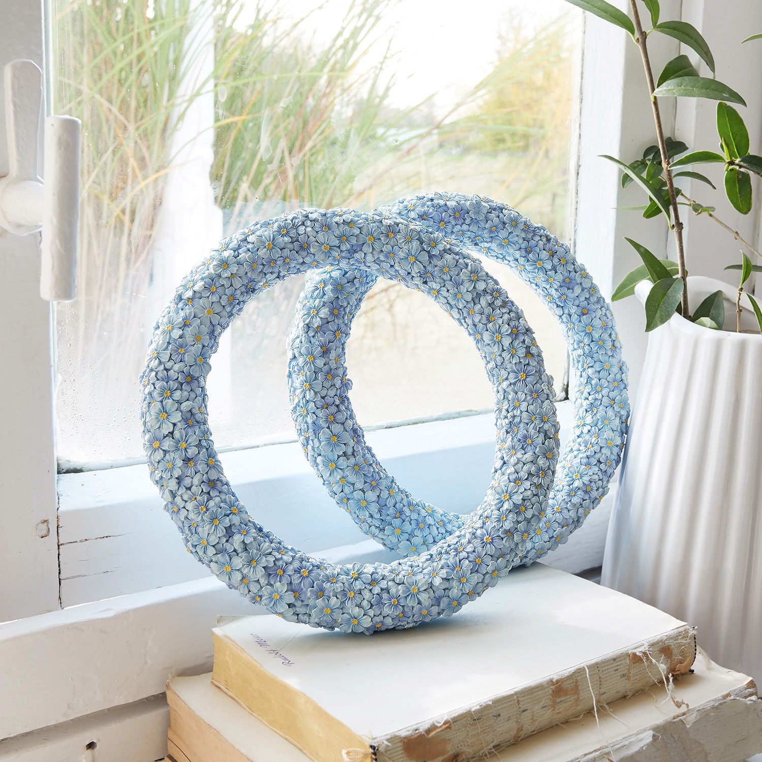 Decoratief blauw bloemenbeeld van hars op boeken bij het raam, woondecoratie