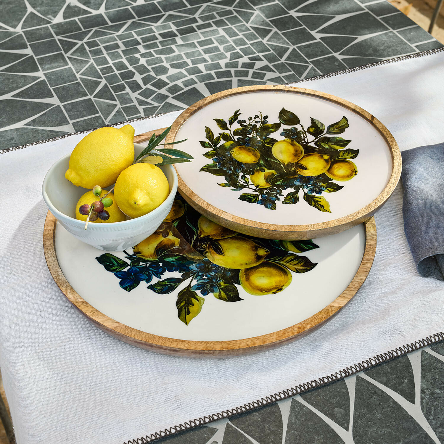 Twee ronde dienbladen van hout en keramiek met citroendesign op witte achtergrond op mozaïektafel