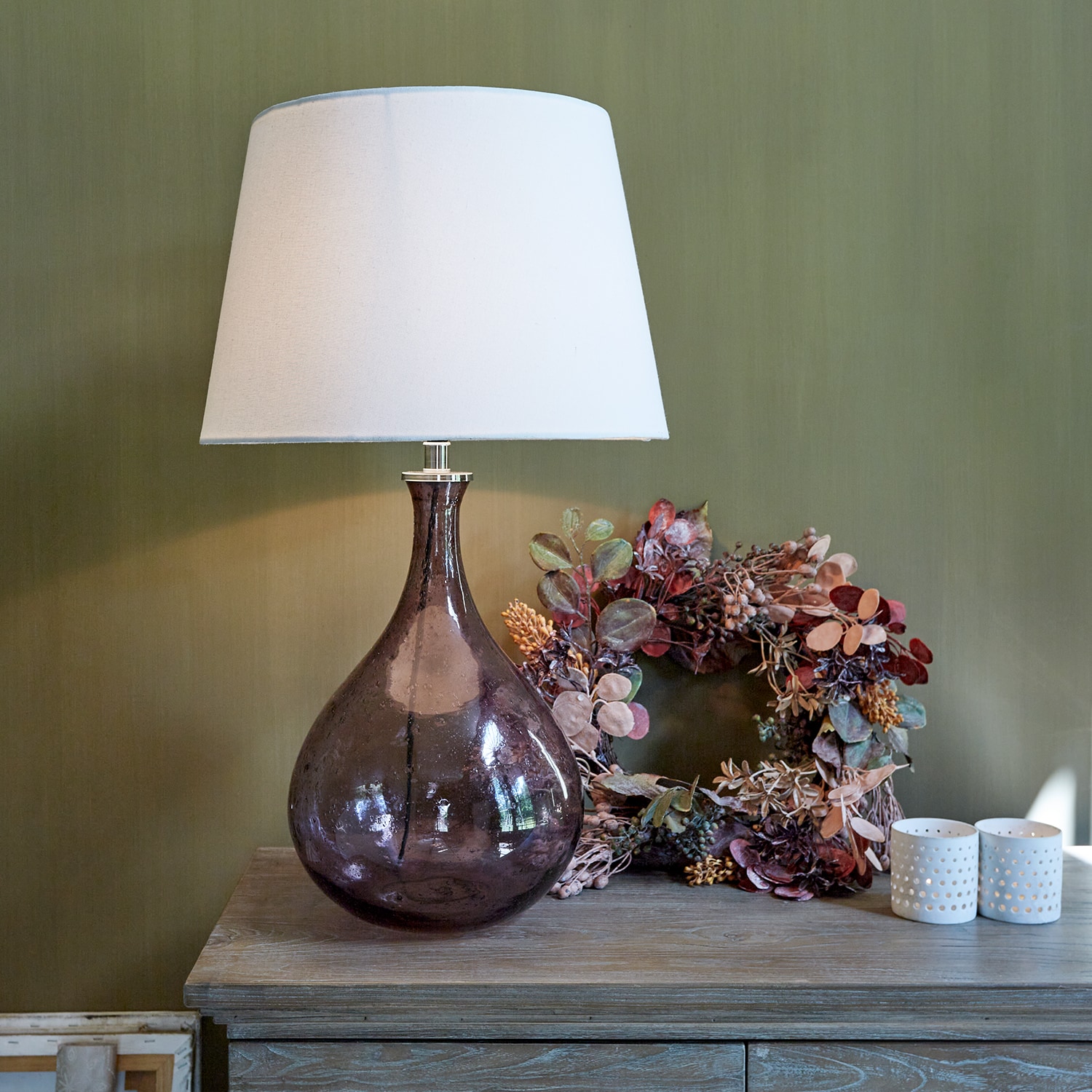 Glazen tafellamp met witte kap en bruine transparante voet op houten tafel met decoratie
