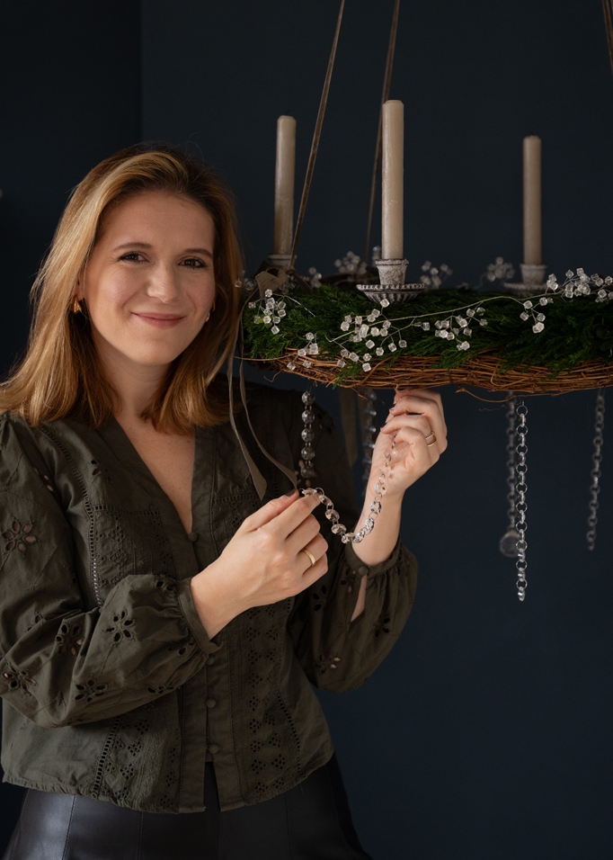 Groene adventskrans met witte kaarsen en kristallen kralen decoratie tegen een donkere achtergrond.