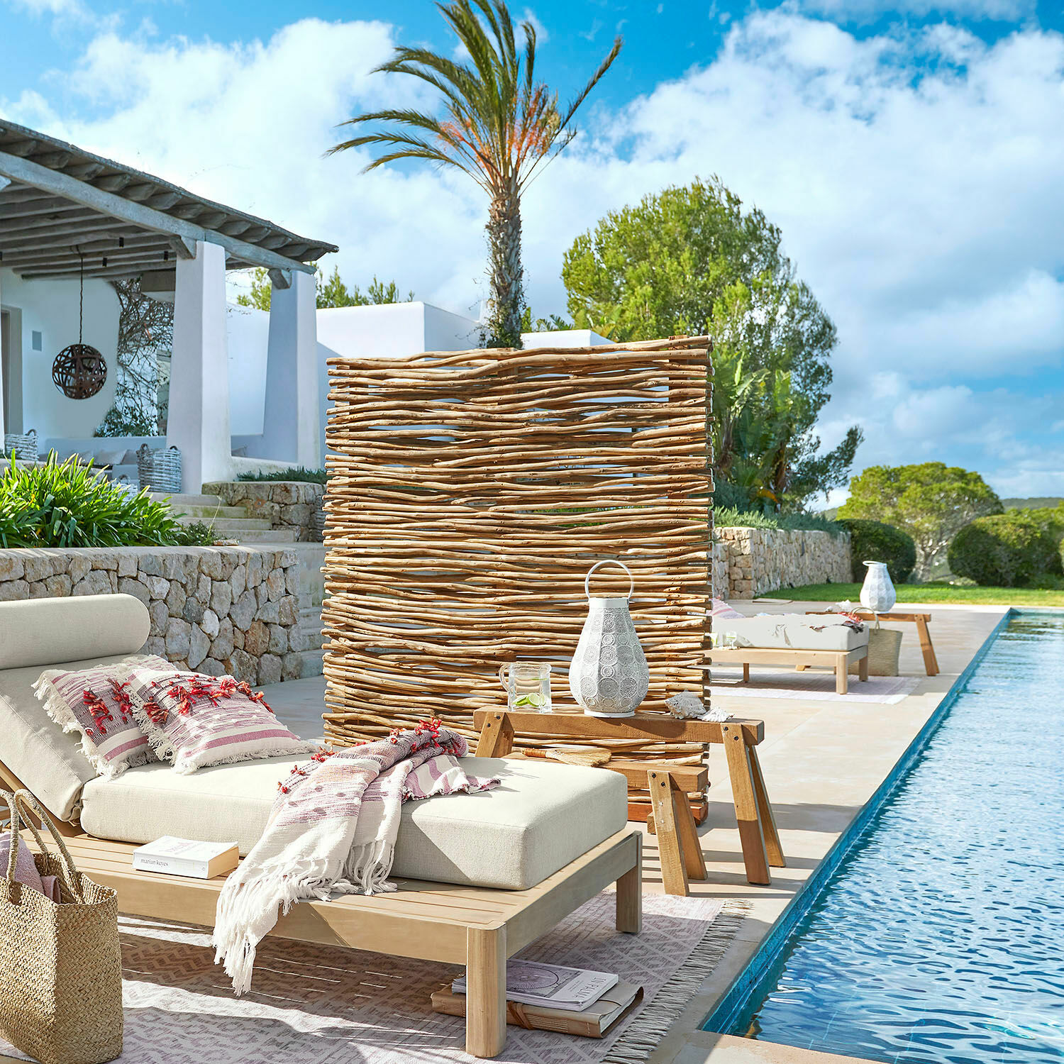 Tuinligstoel met lichtbeige kussen en houten tafel bij het zwembad in boho-stijl