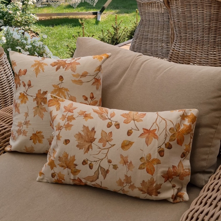 Decoratieve katoenen kussens in beige met herfstbladeren en eikels op een rotan tuinbank