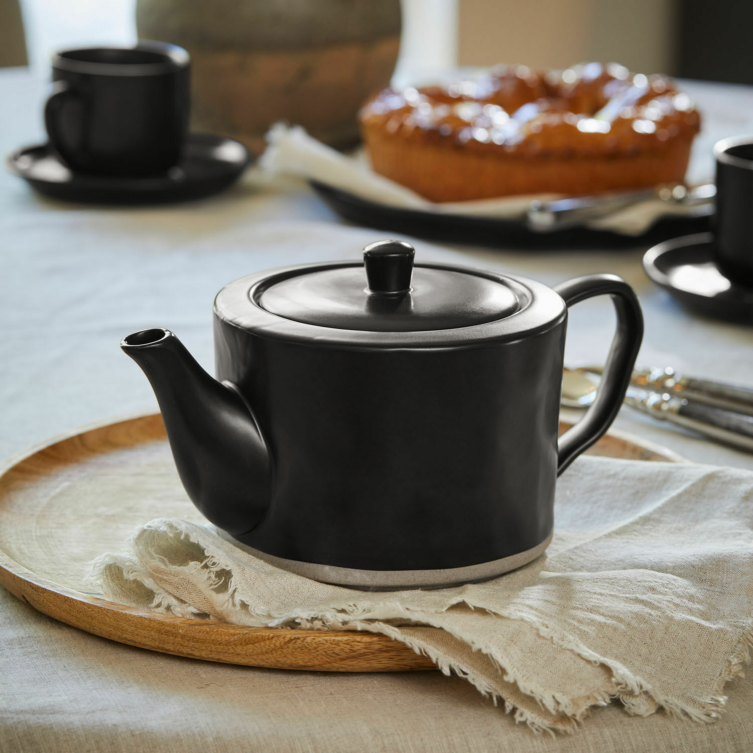 Theepot Biarré Zwarte keramische theepot op houten tafel met bloemen en glazen flessen als decoratie