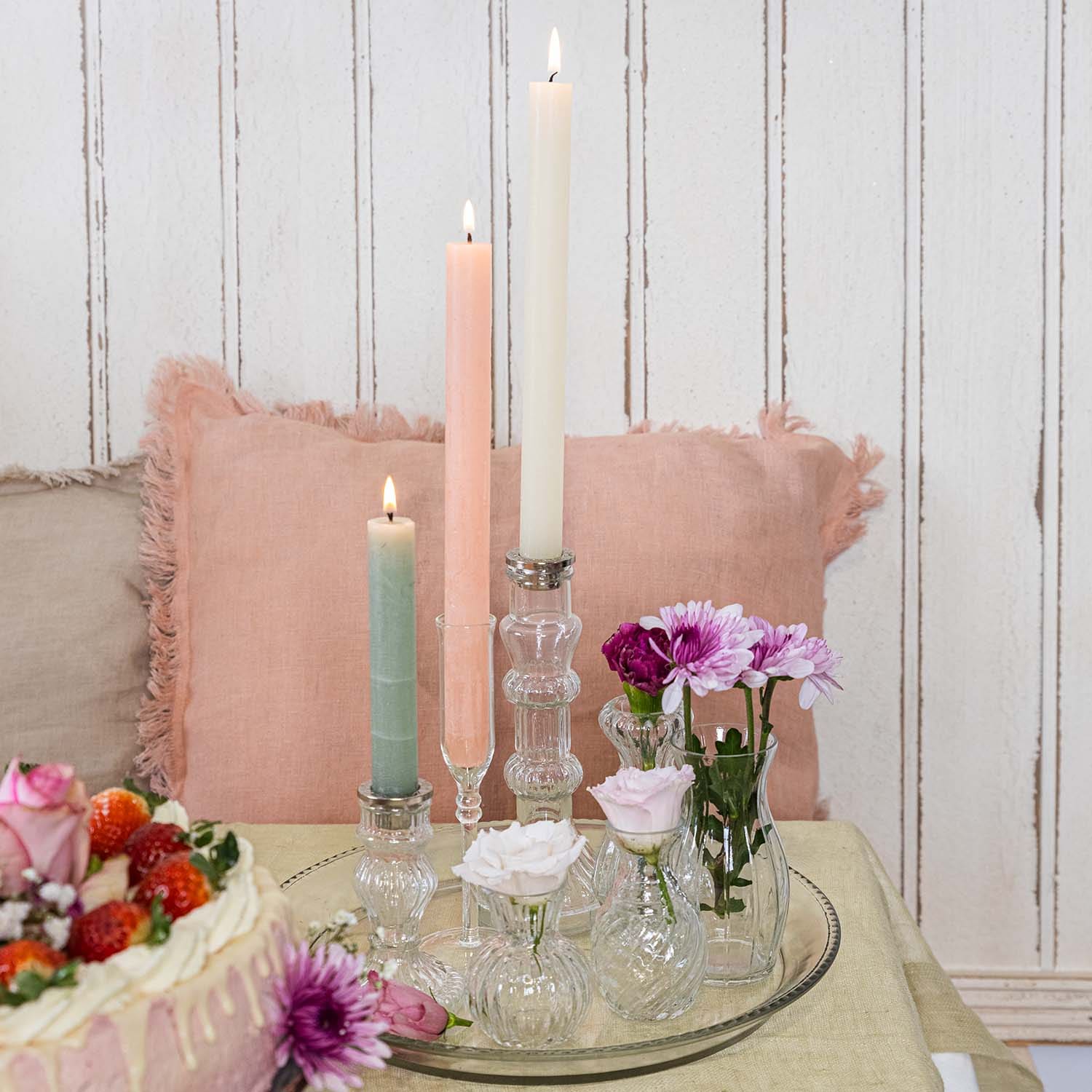 Set pastelkaarsen en kleine glazen vaasjes met bloemen op een glazen dienblad op tafel