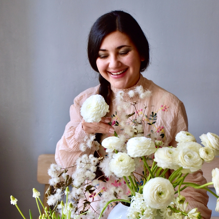 Vrouw in pastel geborduurde blouse met witte bloemen in vaas tegen lichte achtergrond