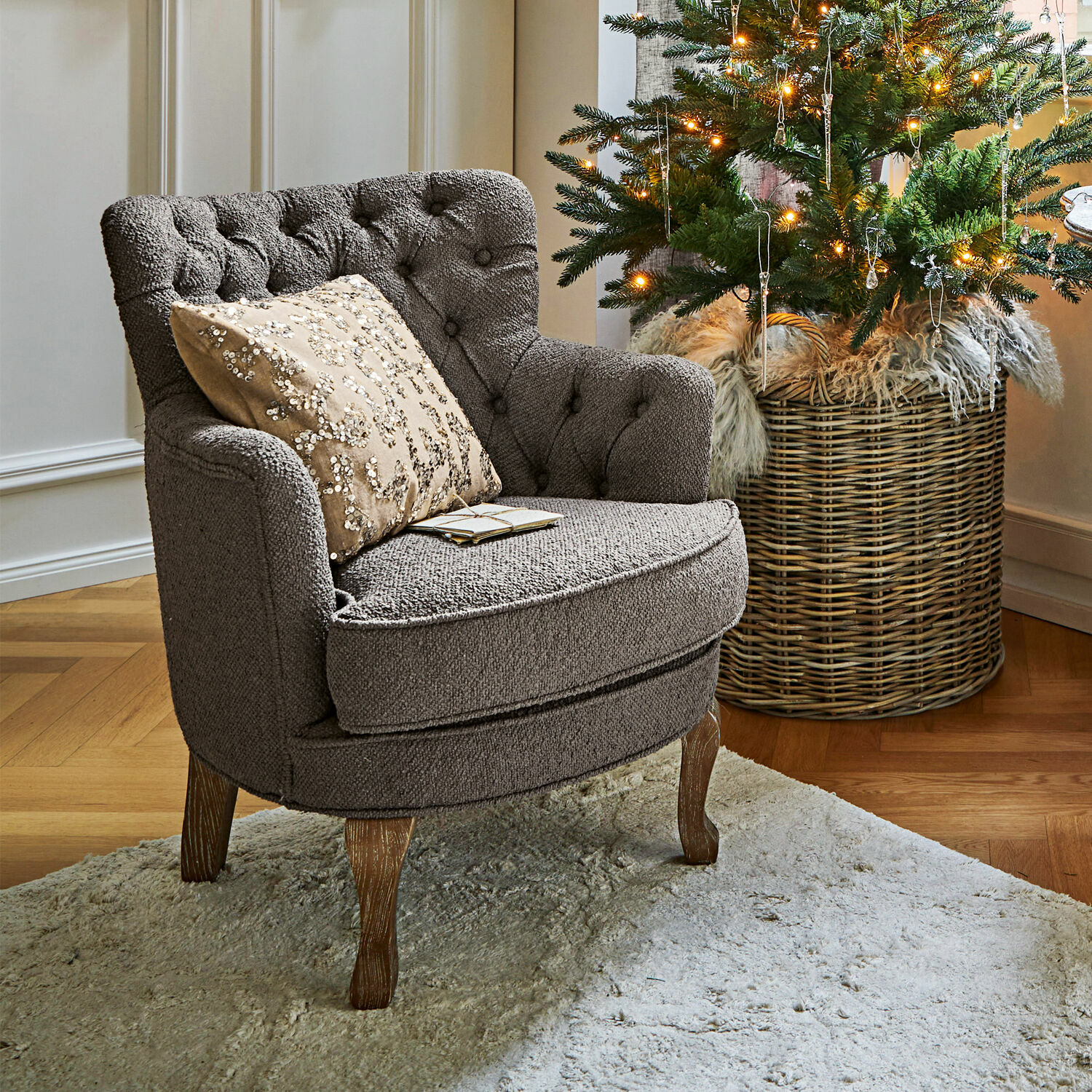 Fauteuil Calgary Grijze gestoffeerde stoel met houten poten op lichte vloerkleed naast versierde kerstboom