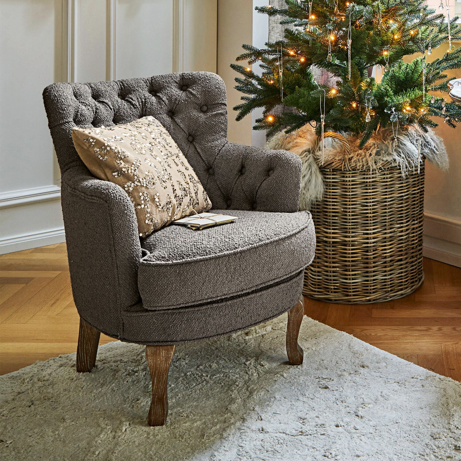 Fauteuil Calgary Grijze gestoffeerde stoel met houten poten op lichte vloerkleed naast versierde kerstboom