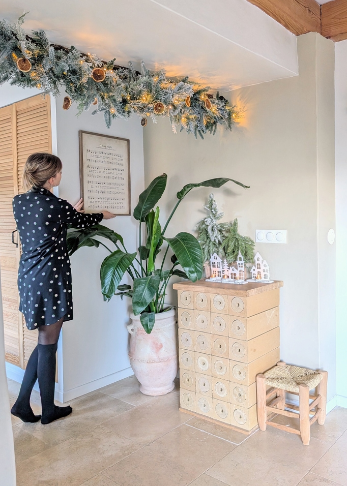 Kerstdecoratie met groene slinger en gedroogde sinaasappelschijfjes in lichte ruimte met planten en houten meubels