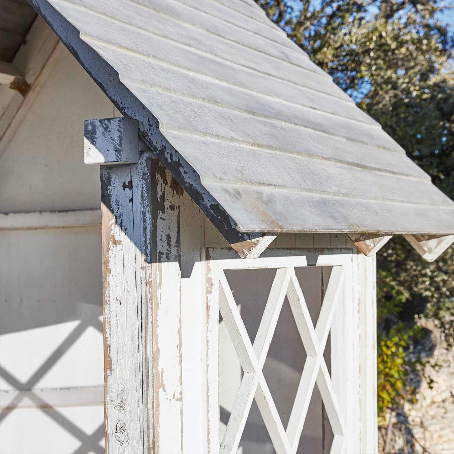 Witte houten tuinhuis met verweerd uiterlijk en schuin dak buiten in rustieke stijl