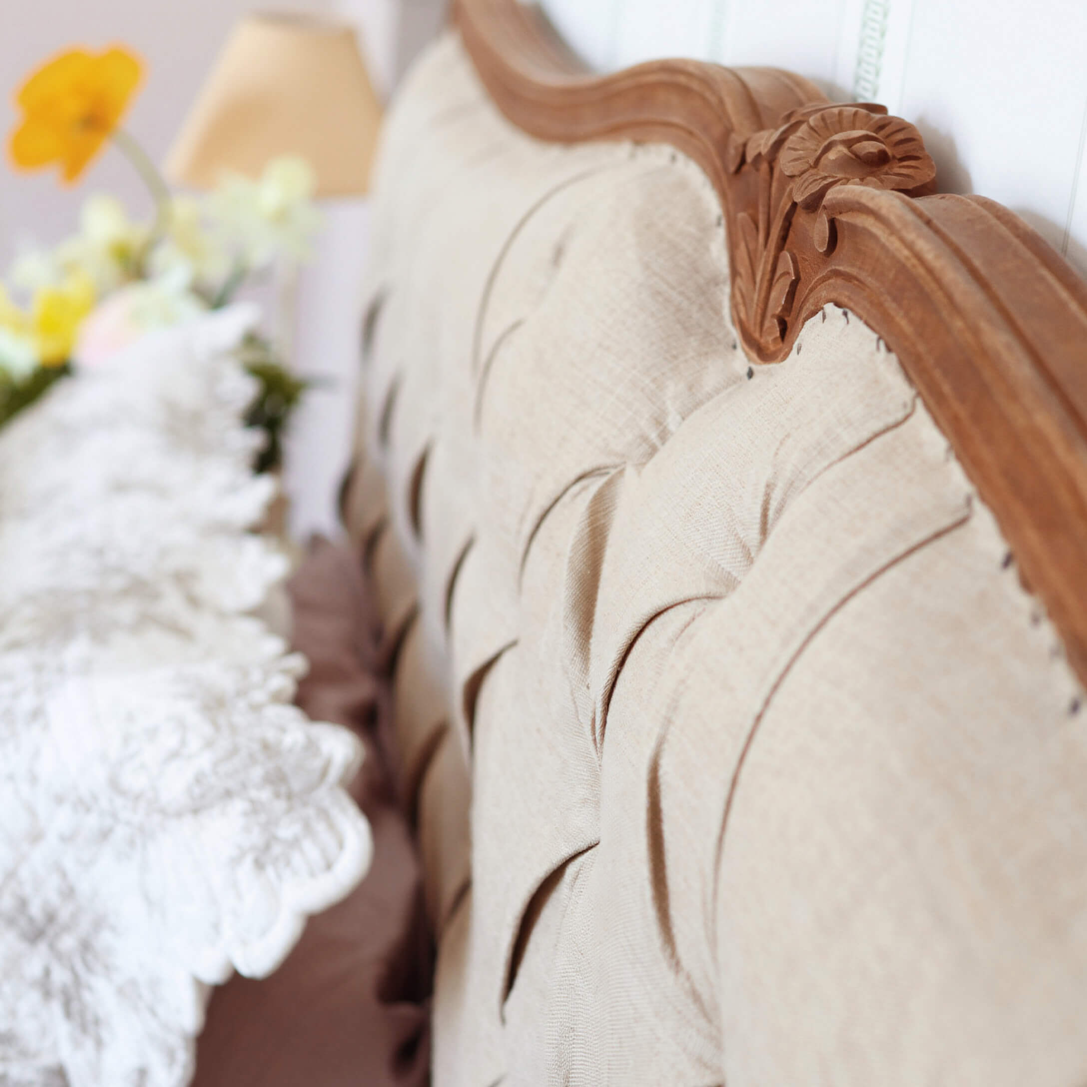 Beige gestoffeerde rugleuning met gesneden houten lijst en decoratief kussen op de achtergrond