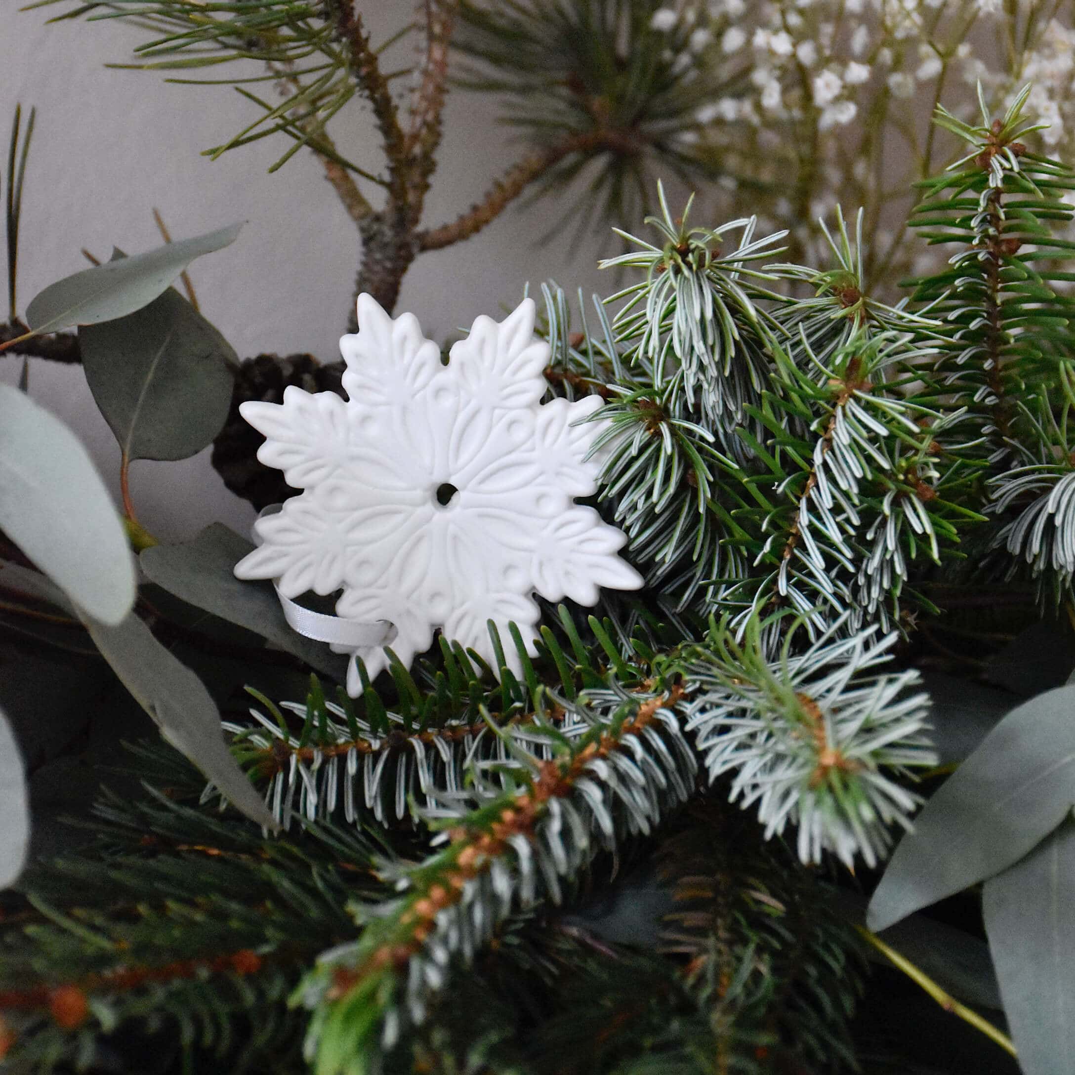 Witte keramische kerstversiering in sneeuwvlokvorm op groene dennentakken