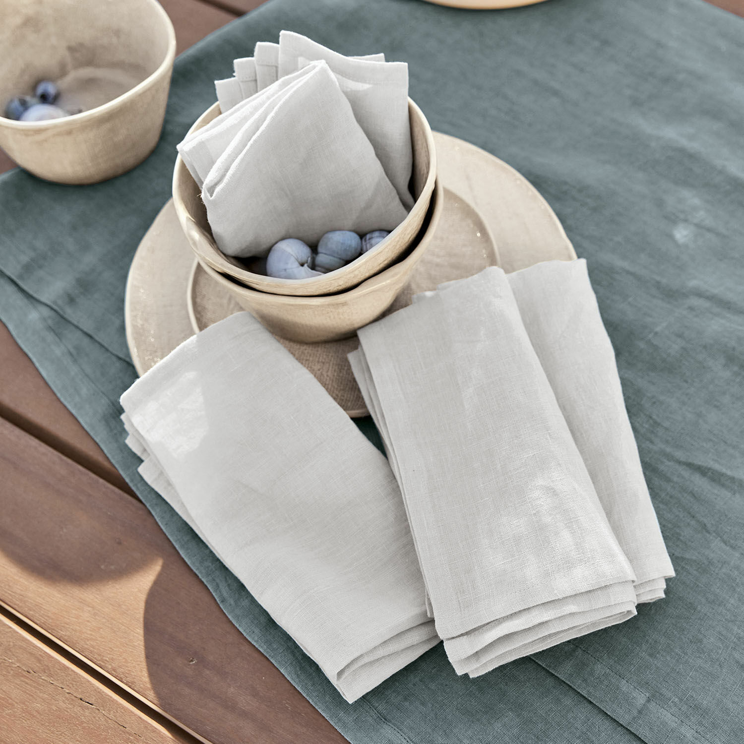 Witte linnen servetten op groene tafelkleed met keramische kommen en decoratieve ballen