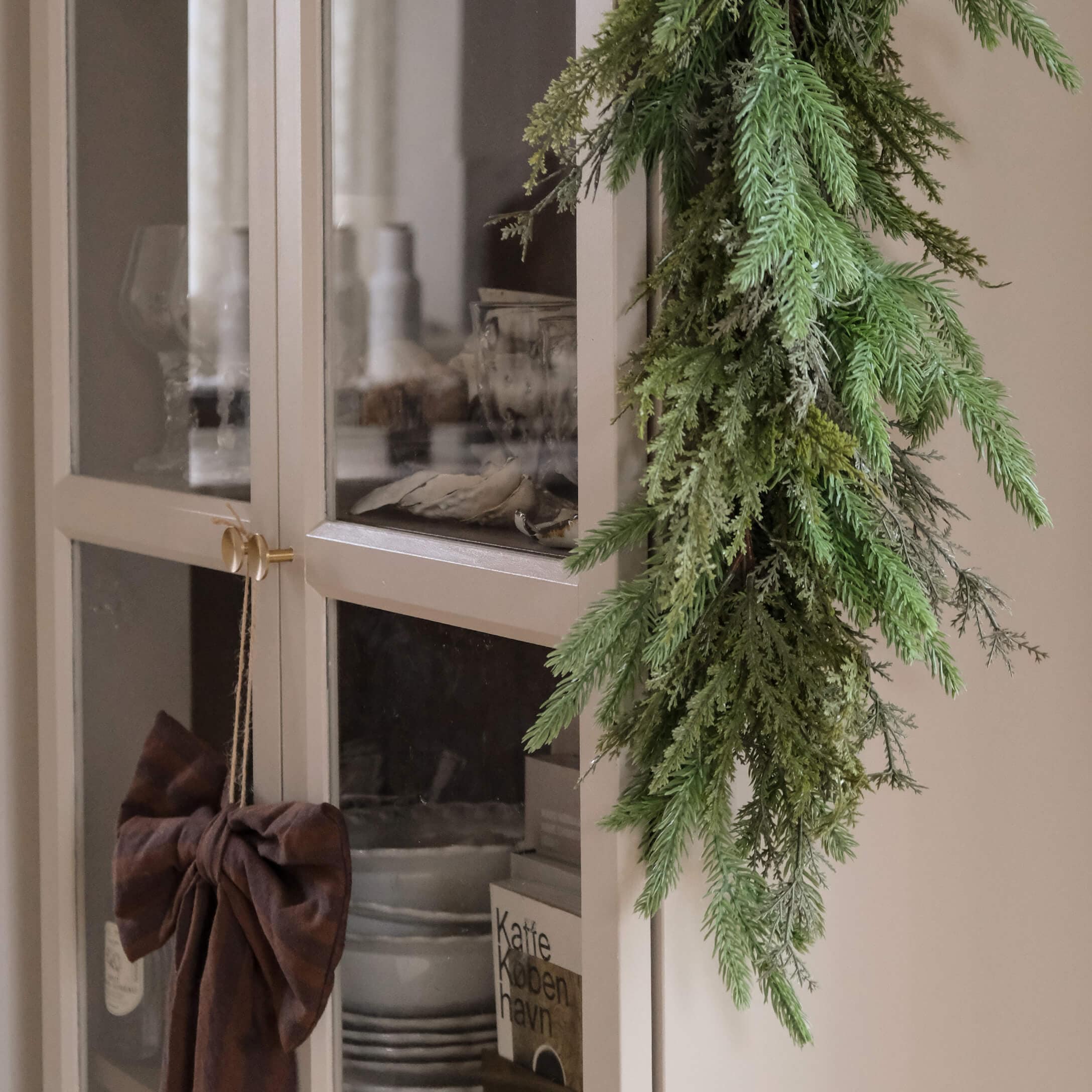 Decoratieve groene takkenkrans aan een lichte kast met glazen deuren in Scandinavische stijl
