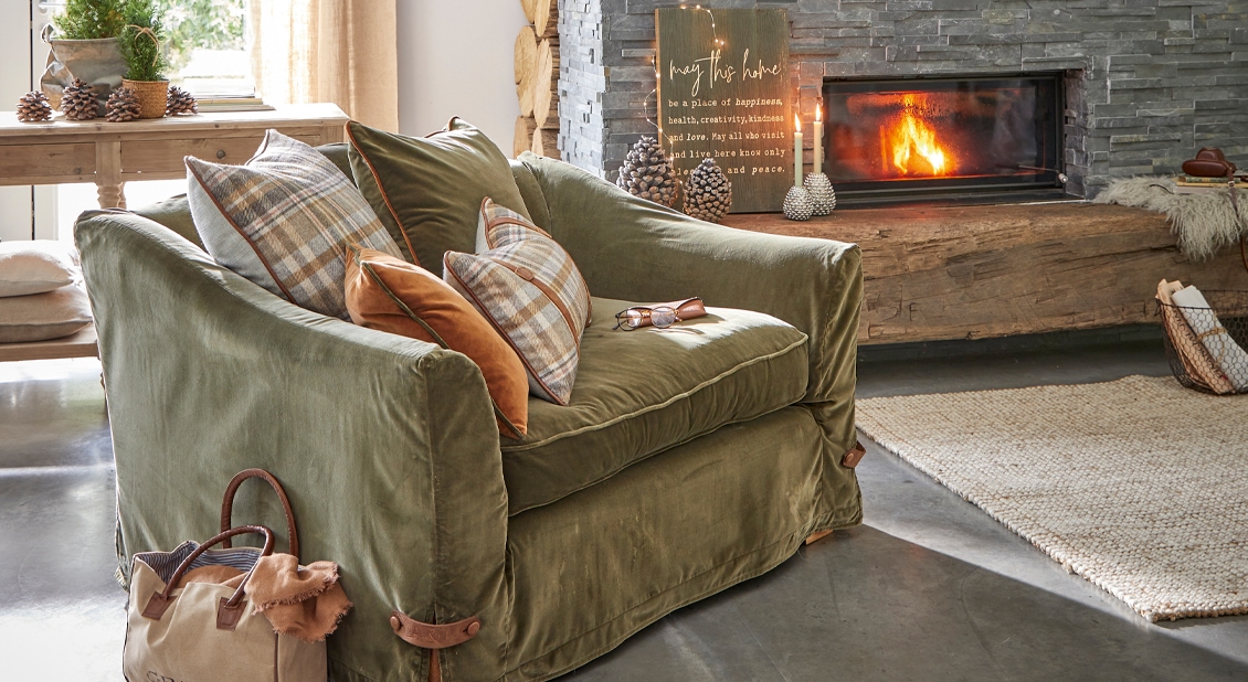 Groene fluwelen bank met geruite kussens bij open haard in gezellige woonkamer