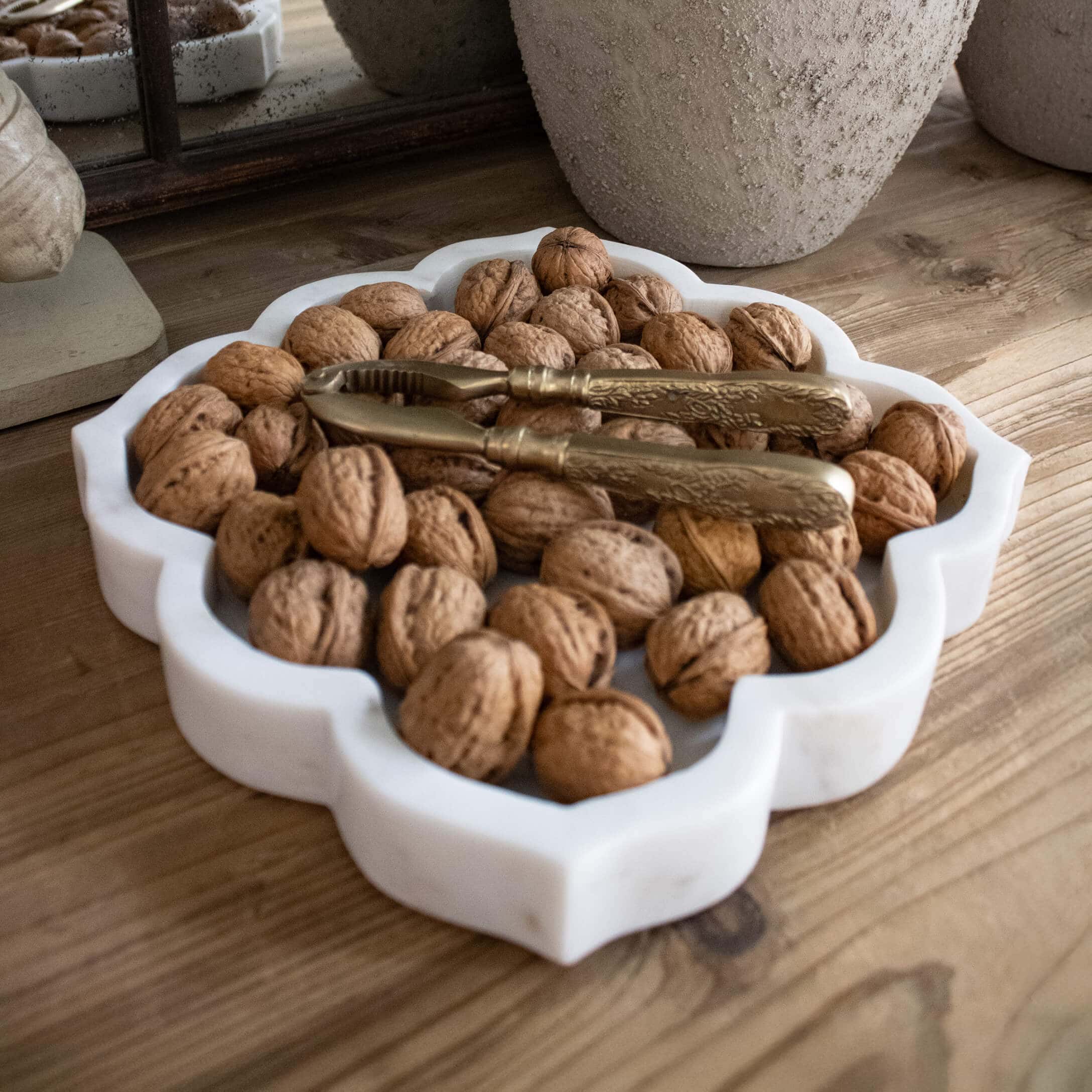 Witte marmeren schaal met walnoten en gouden notenkraker op houten tafel