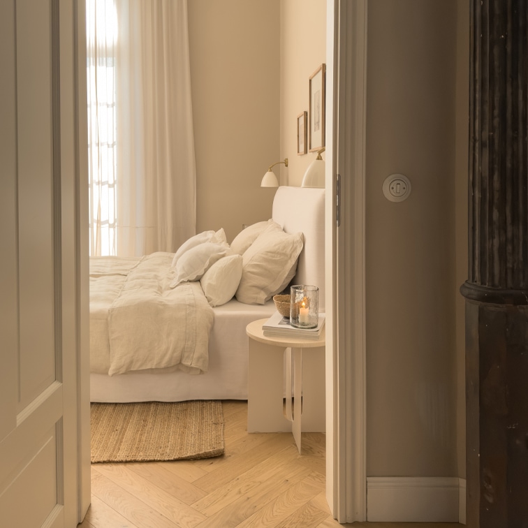 Gezellige slaapkamer in lichte beige tinten met bed en natuurlijke vloerkleed op lichte houten vloer