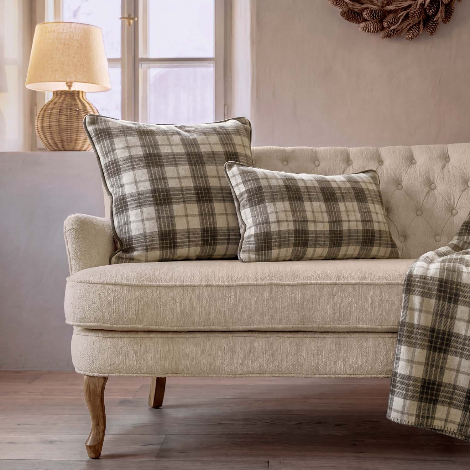 Beige bank met twee geruite kussens in grijs en crème, rotan lamp bij raam in woonkamer