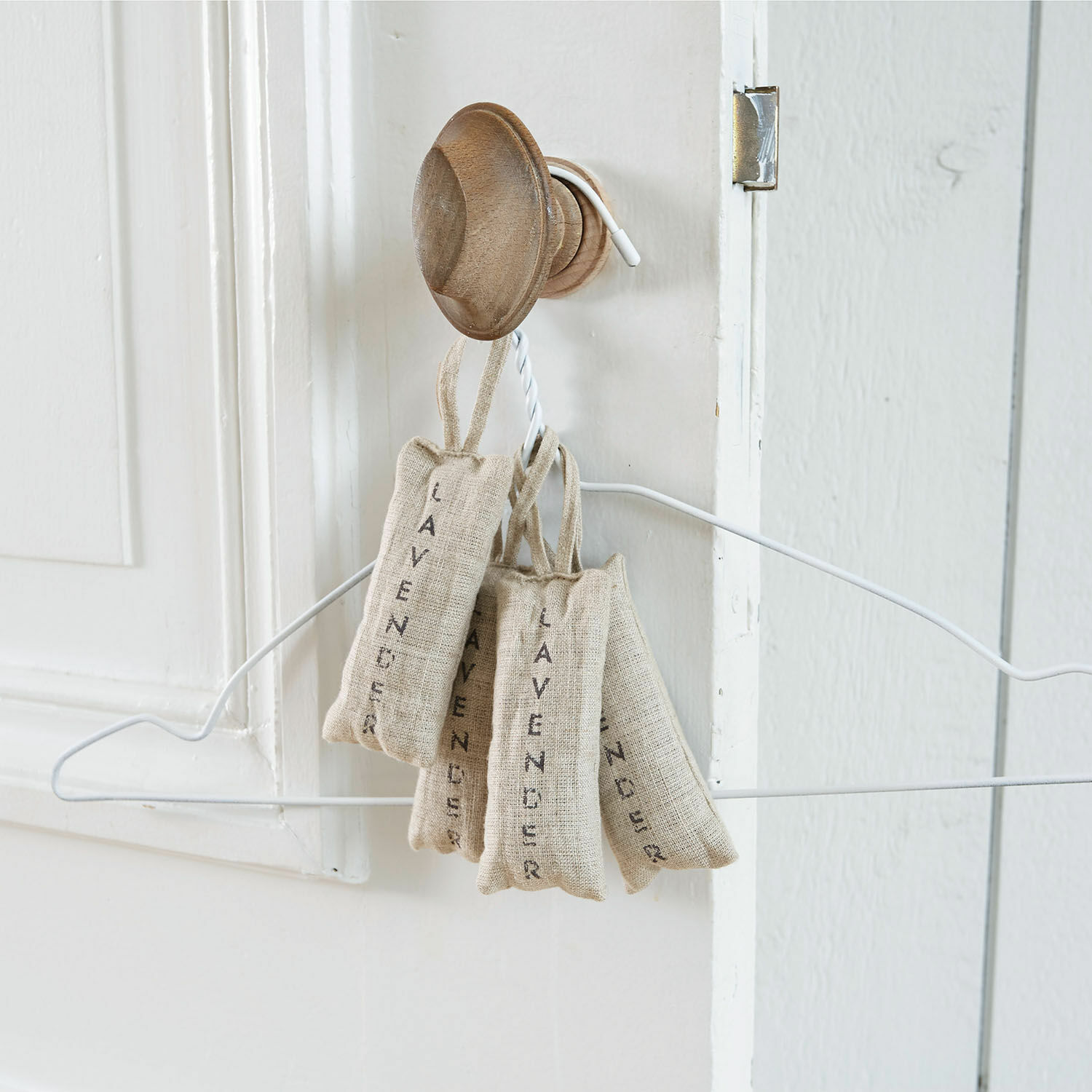 Linnen zakjes met lavendel in natuurlijke kleur aan houten haak aan witte deur