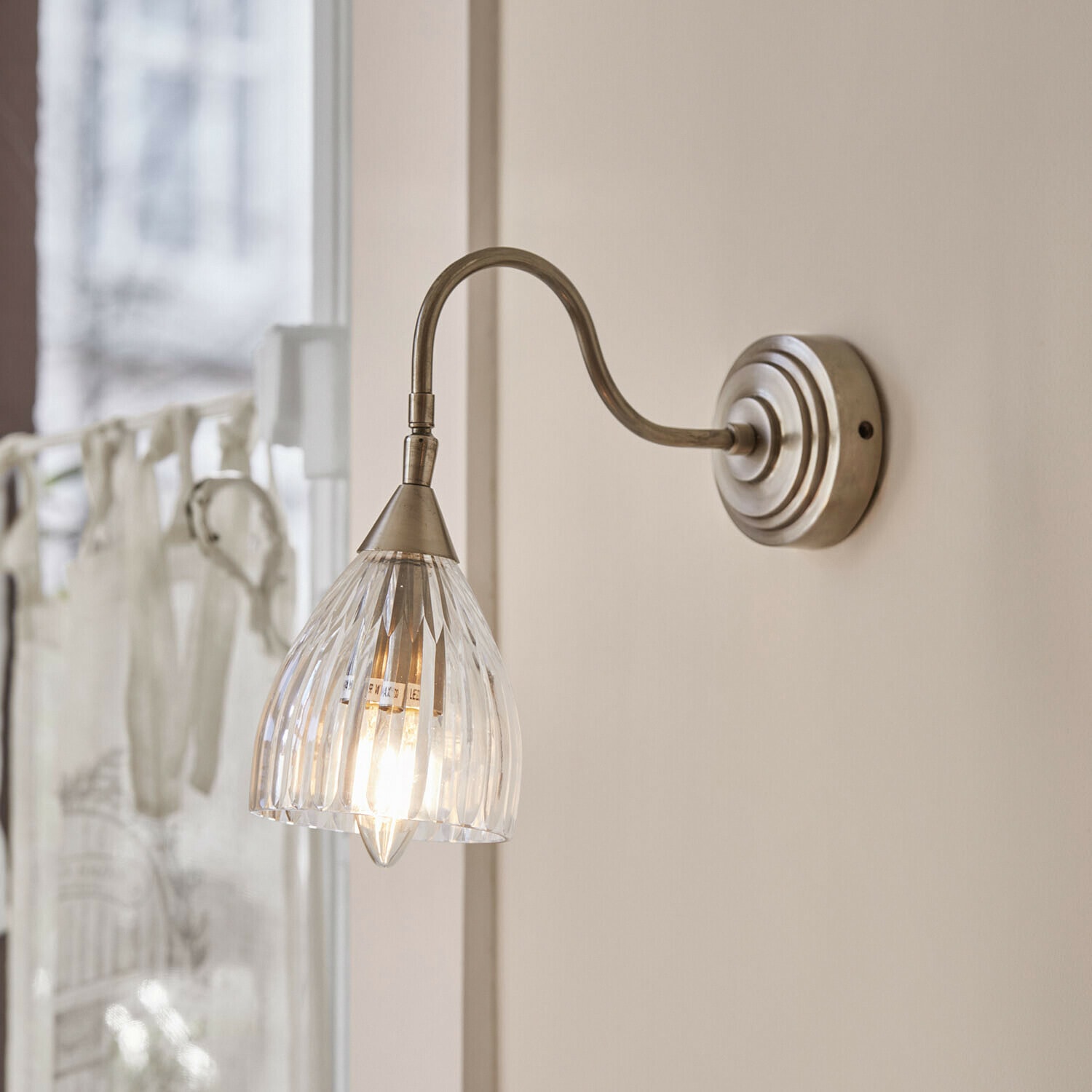 Wandlamp met doorzichtige glazen kap en metalen arm in antiek zilverkleurig ontwerp
