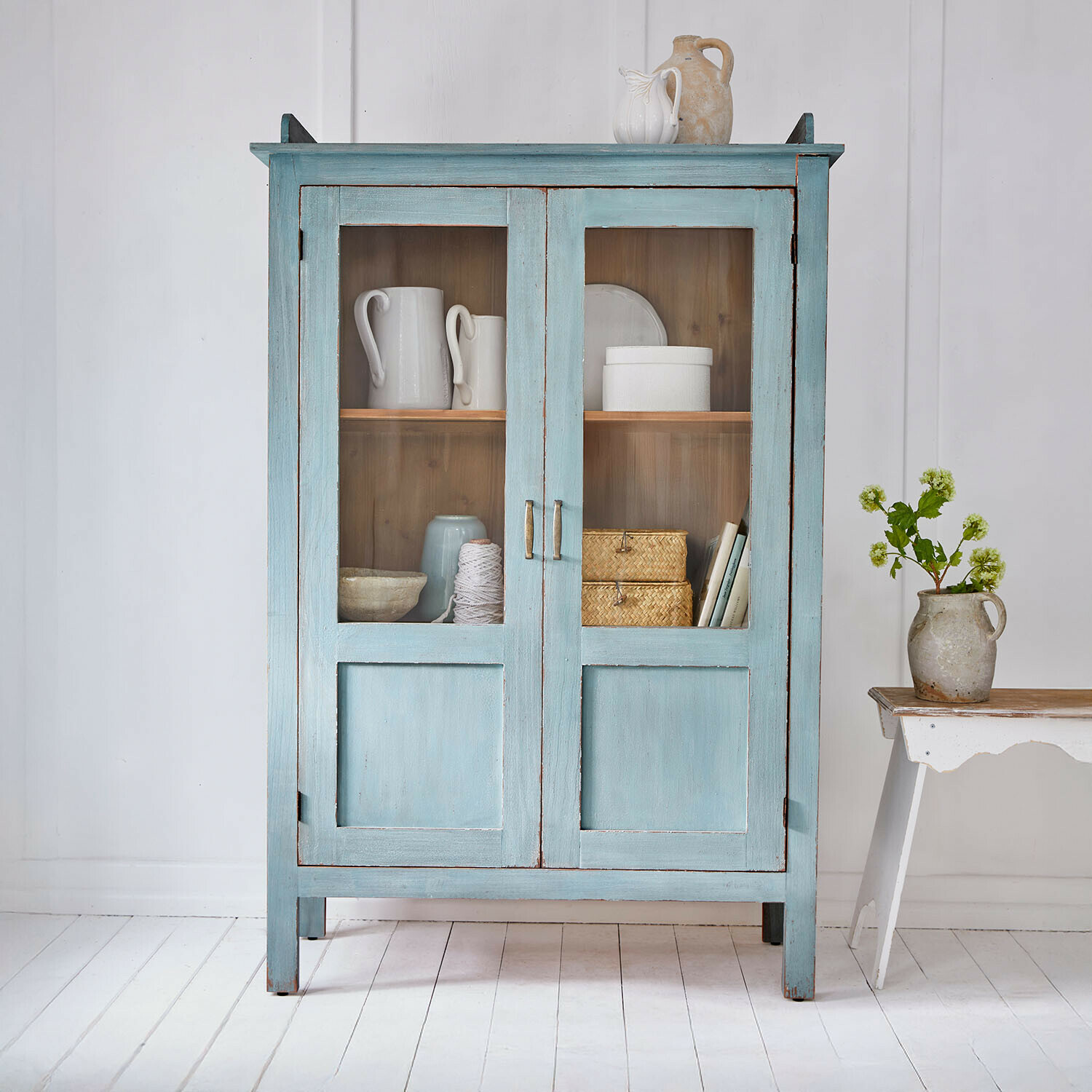 Vitrinekast Nouvellese Blauwe houten kast met glazen deuren en vintage keramische decoraties in lichte kamer
