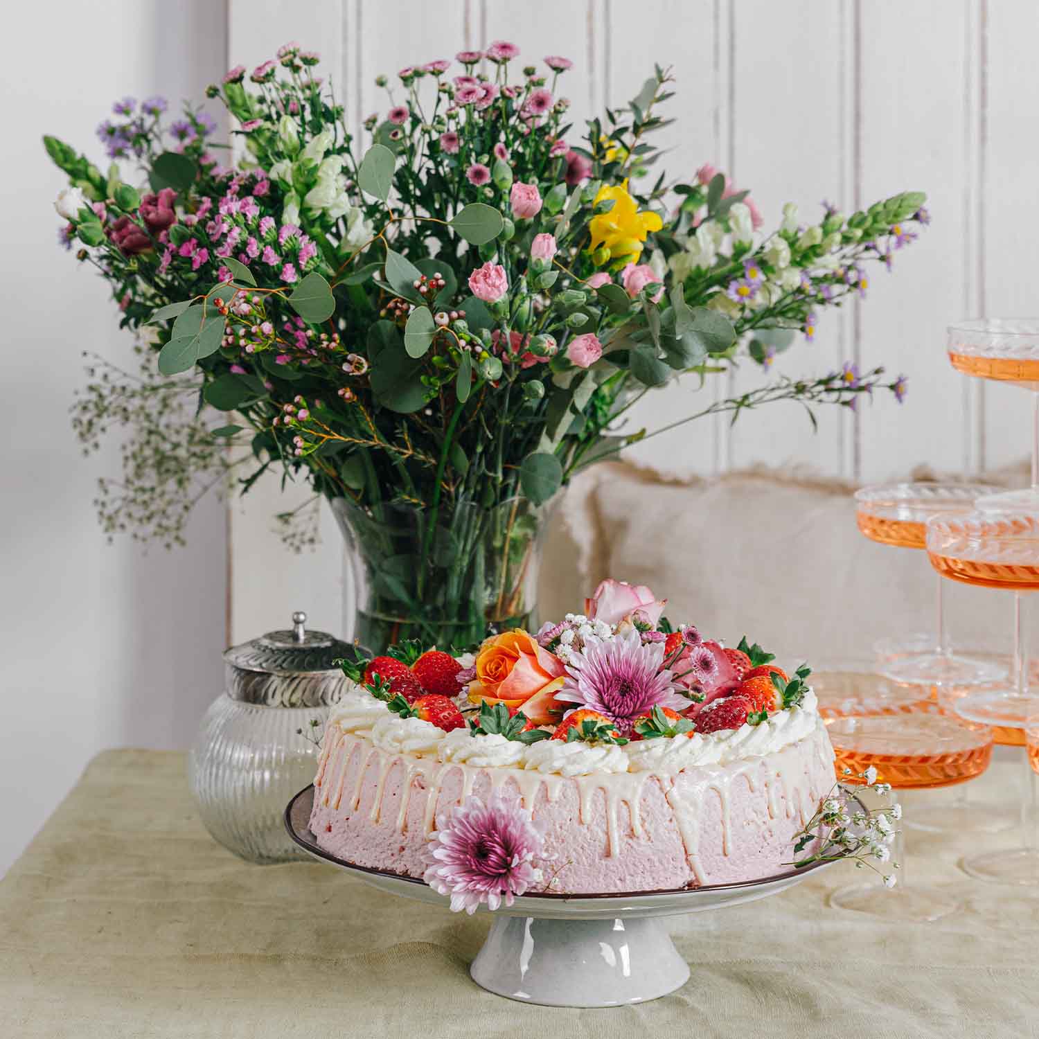 Roze roomtaart met verse aardbeien en bloemen op een witte standaard met boeket op de achtergrond