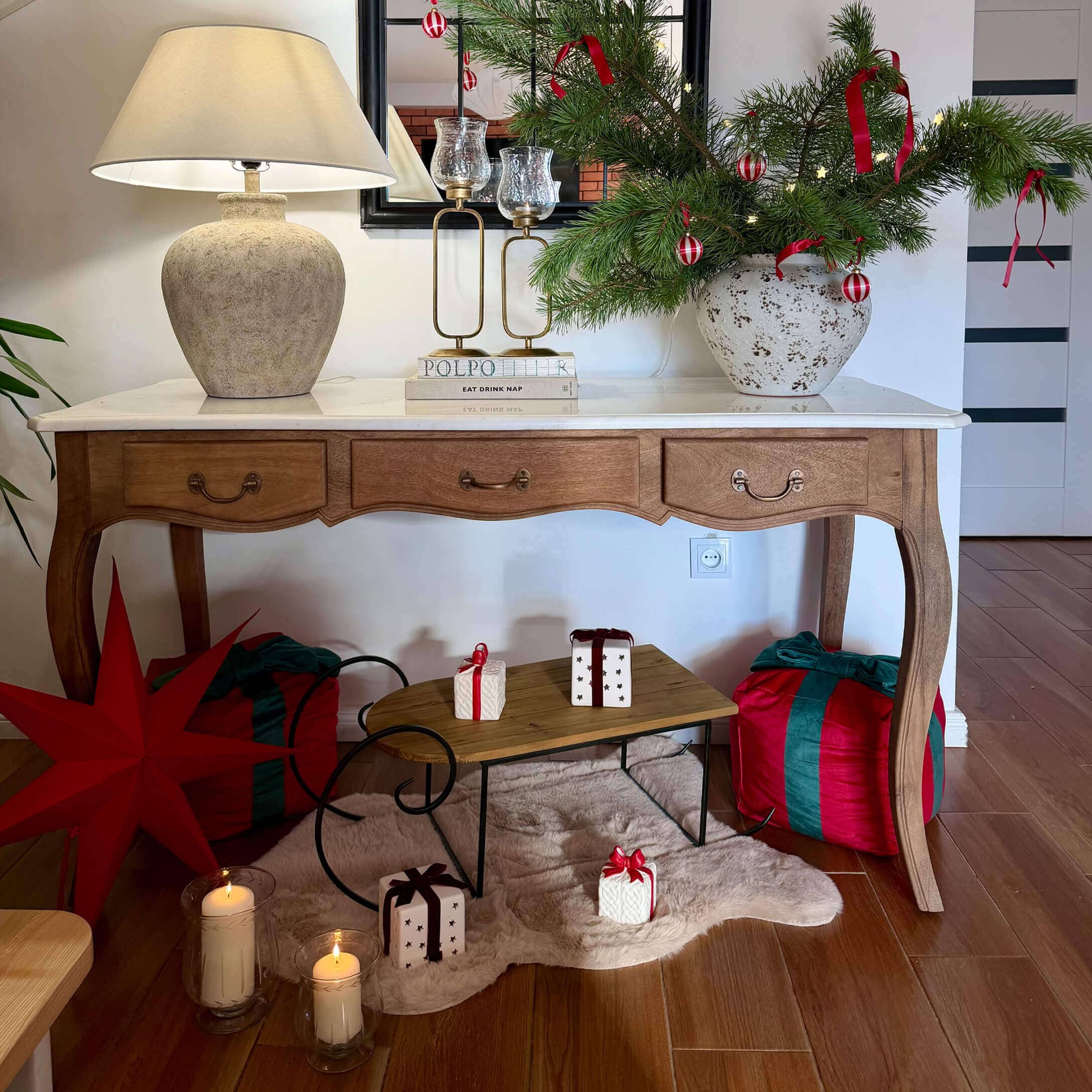 Houten tafel met wit blad, lamp en kerstdecoratie met groene takken en rode linten