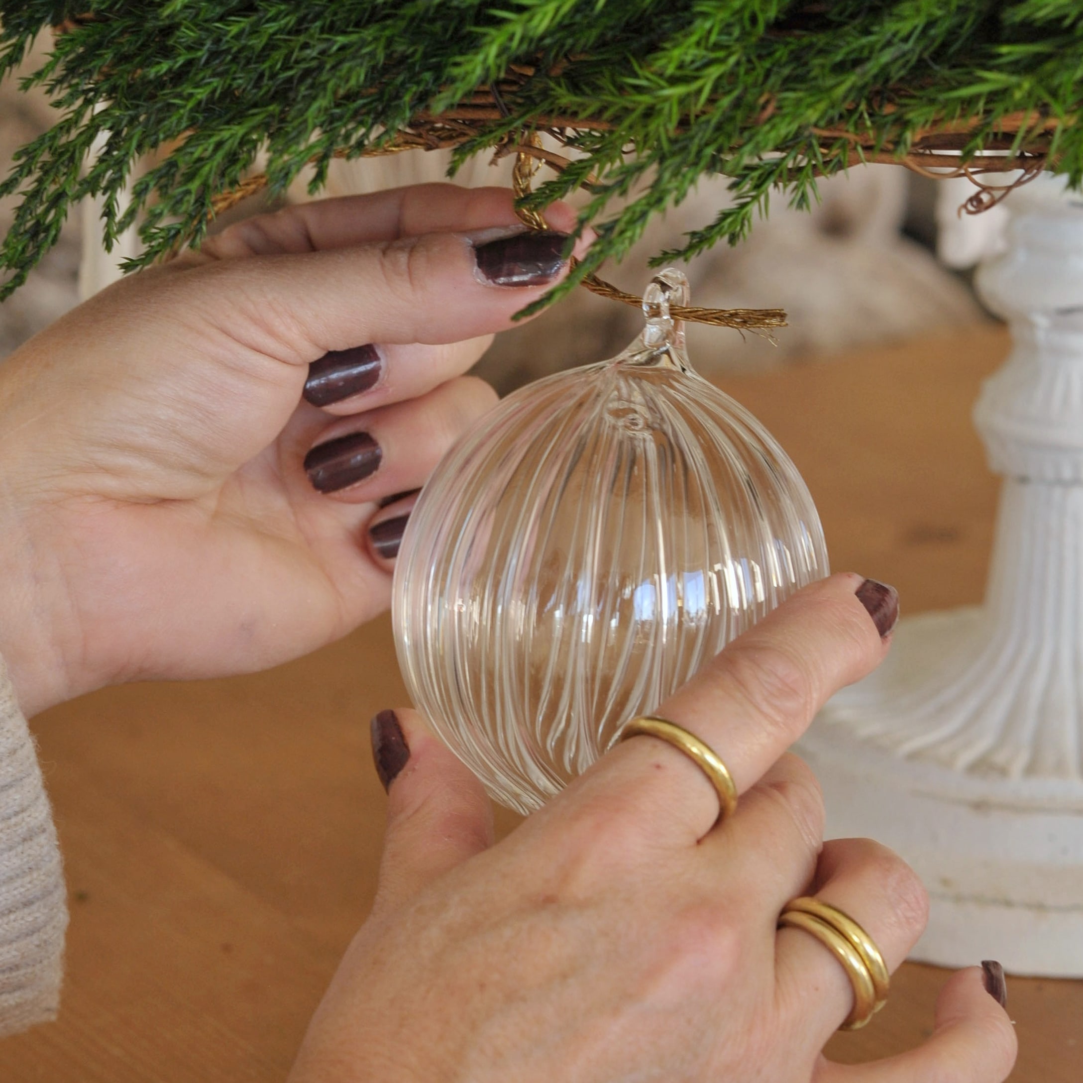Transparante geribbelde glazen kerstbal hangend aan een groene tak van kerstdecoratie