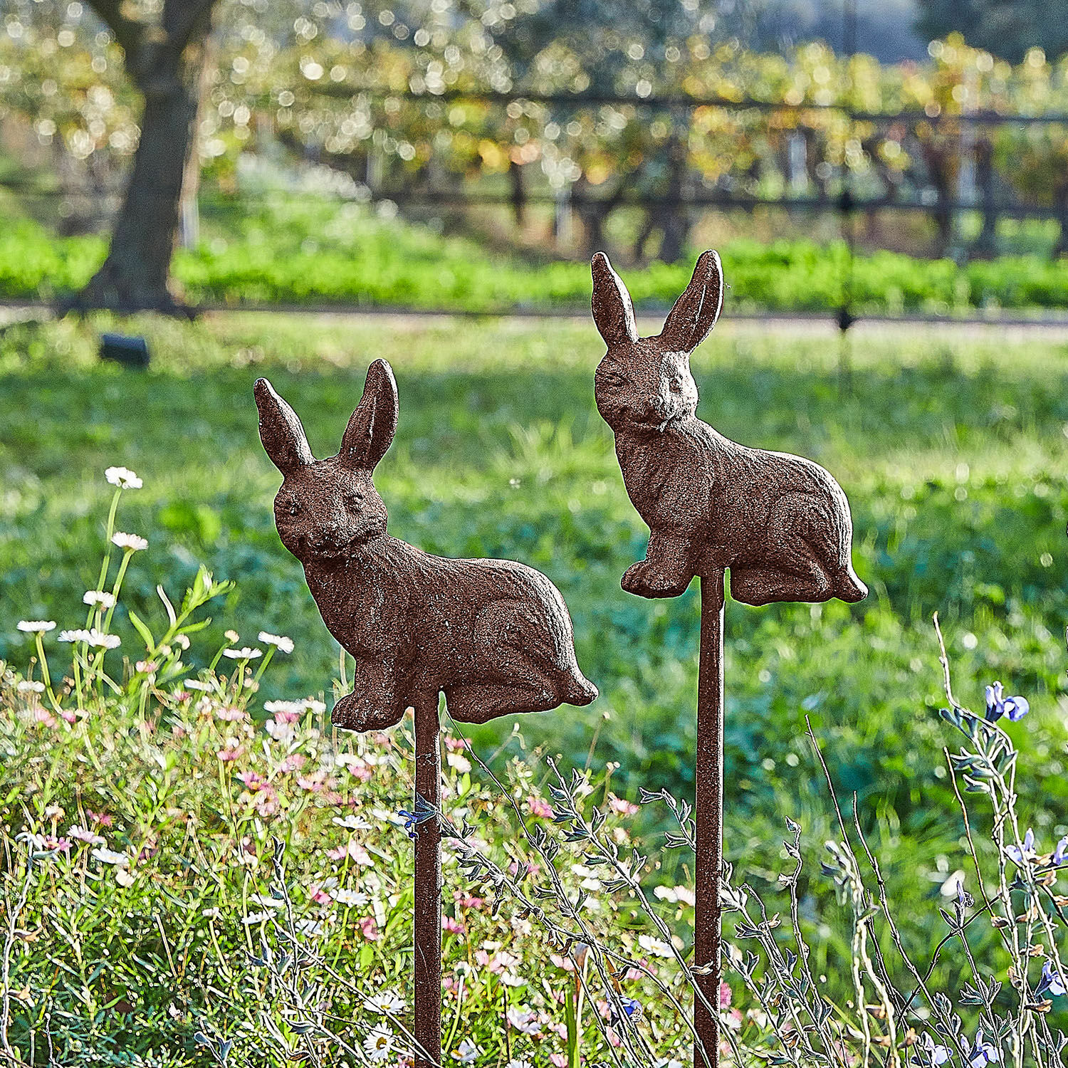 Tuinprikker set van 2 Dariyah Decoratieve tuinpalen met roestige metalen konijnen tegen een achtergrond van groen en bloemen
