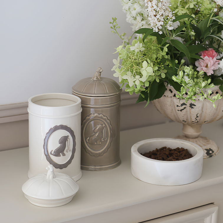 Keramische hondenvoerblikken in crème en beige naast een witte voerbak met brokjes en bloemen