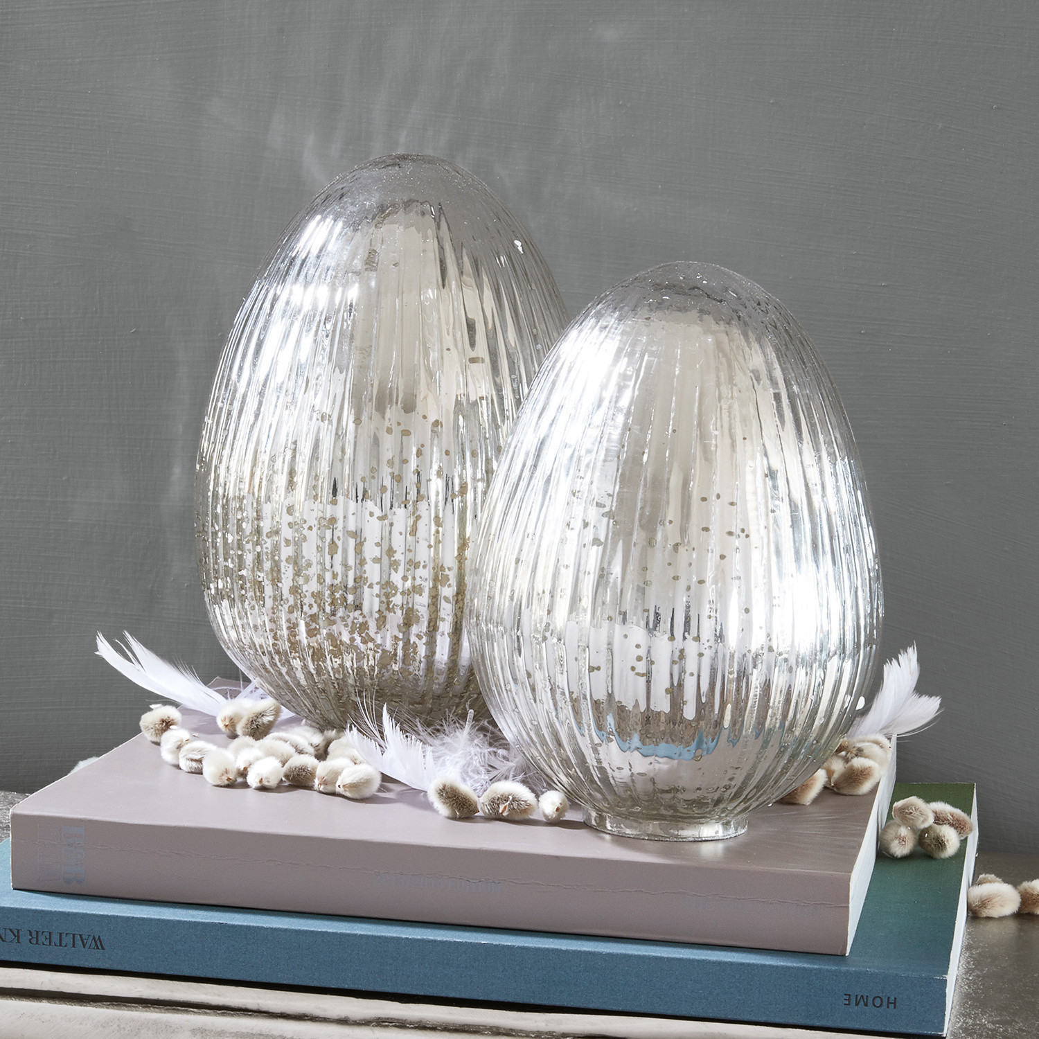 Paasei set van 2 Duvera Twee decoratieve zilverkleurige glazen kandelaars op boeken, versierd met veren en katjes