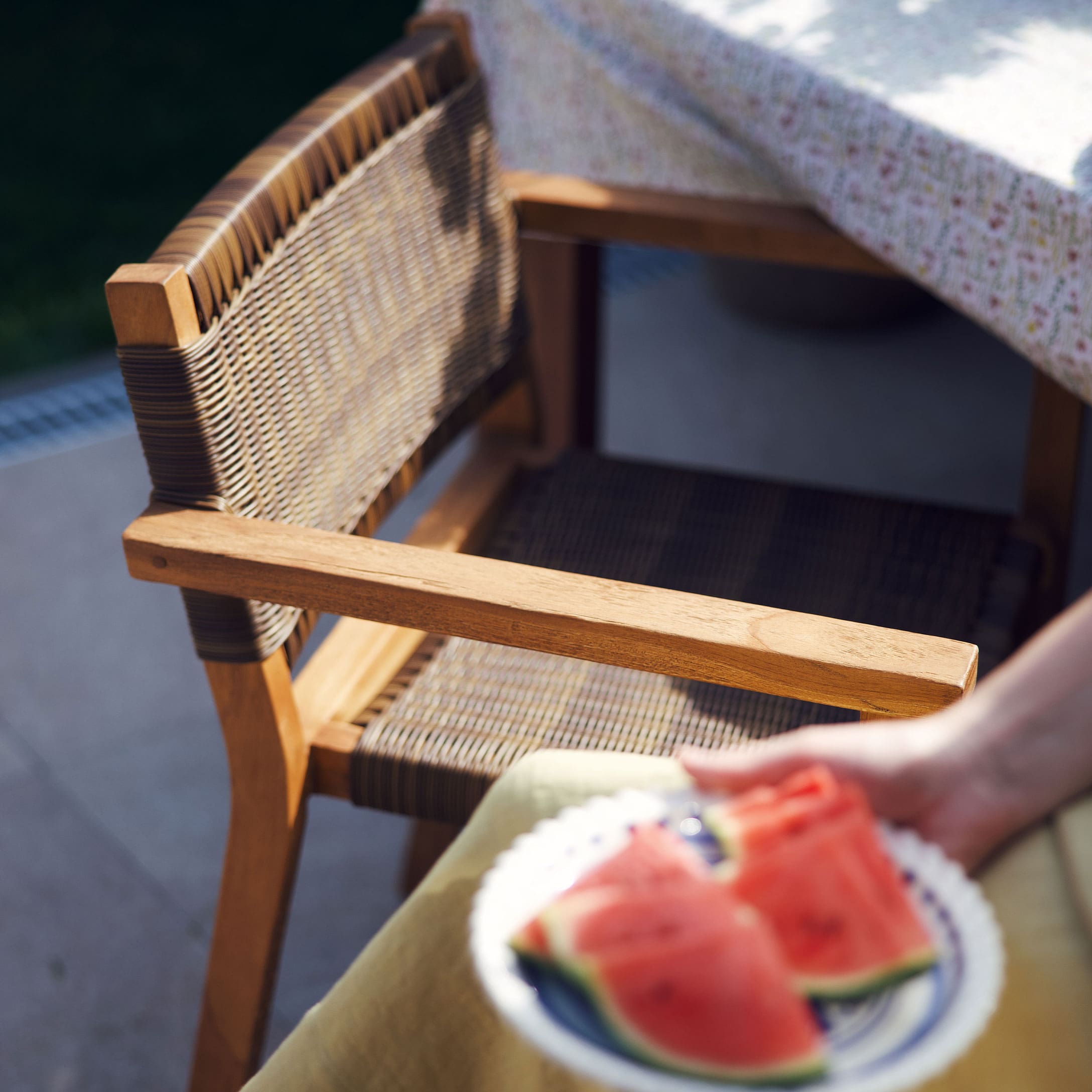 Tuinstoel van hout en natuurlijk vlechtwerk bij een tafel met tafelkleed