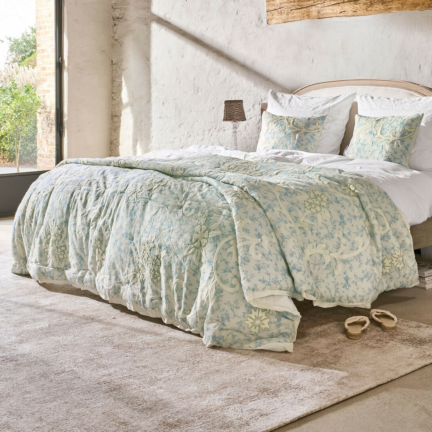 Beddengoed van zachte stof met lichtblauwe en crèmekleurige bloemenpatronen in lichte kamer