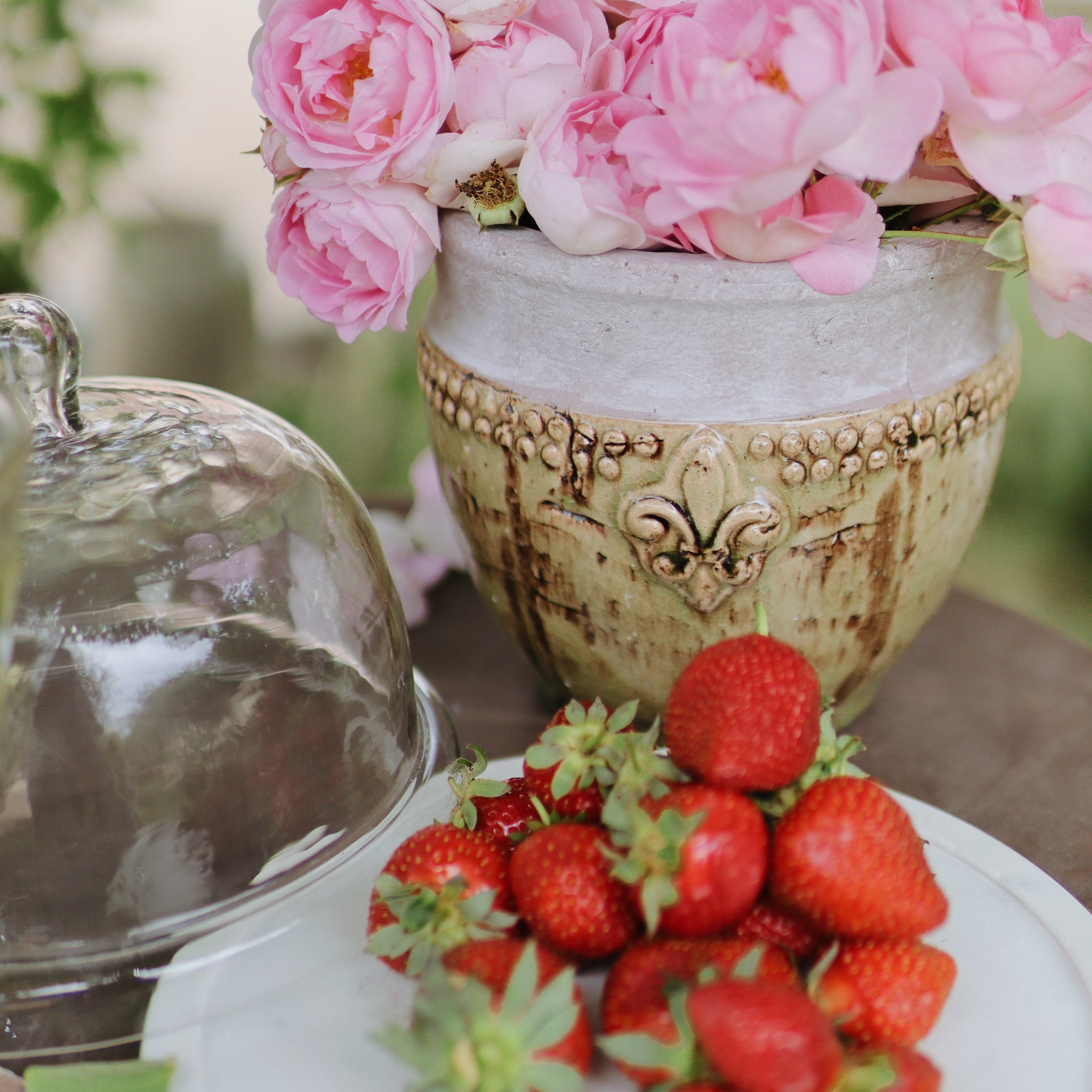 Keramische pot met roze bloemen en verse aardbeien op een wit bord