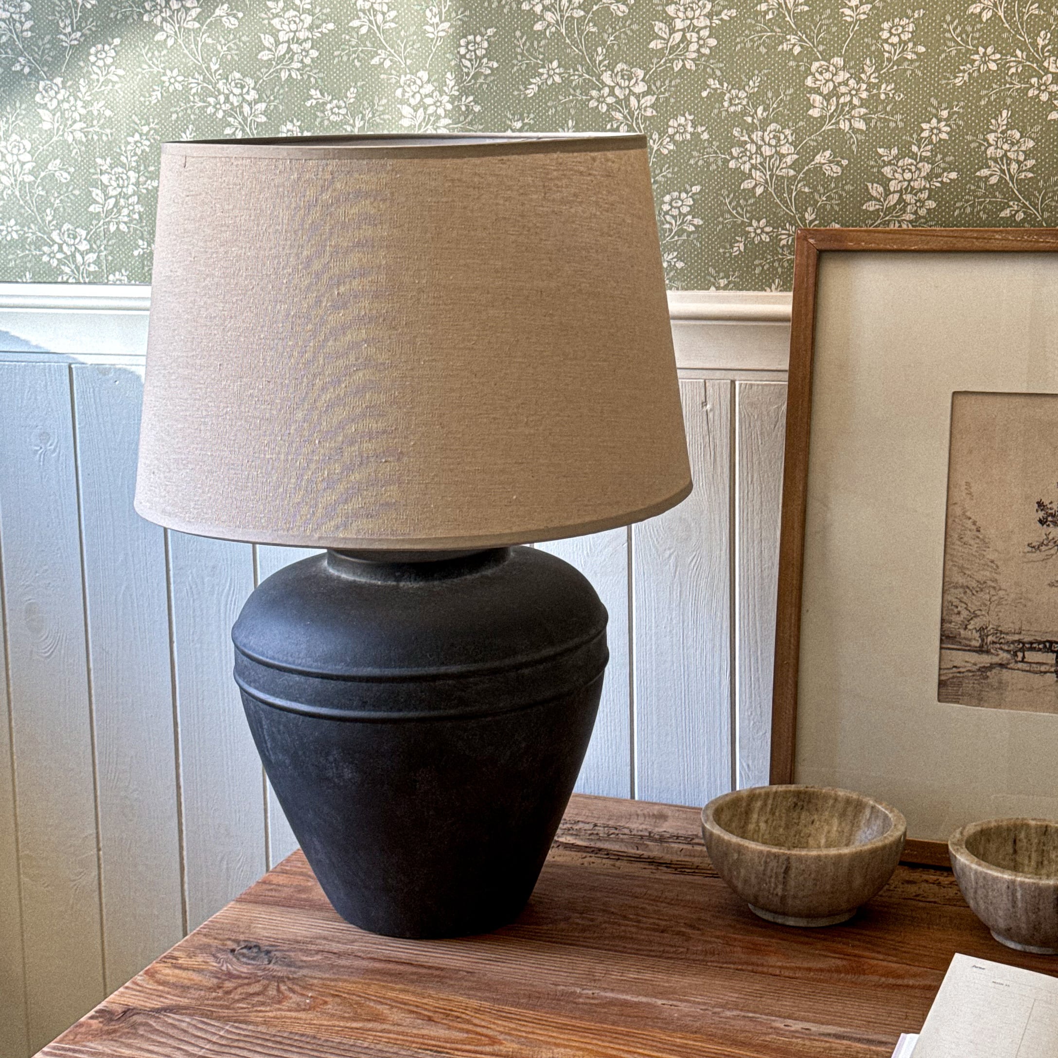 Tafellamp met zwarte keramische voet en beige lampenkap op houten tafel