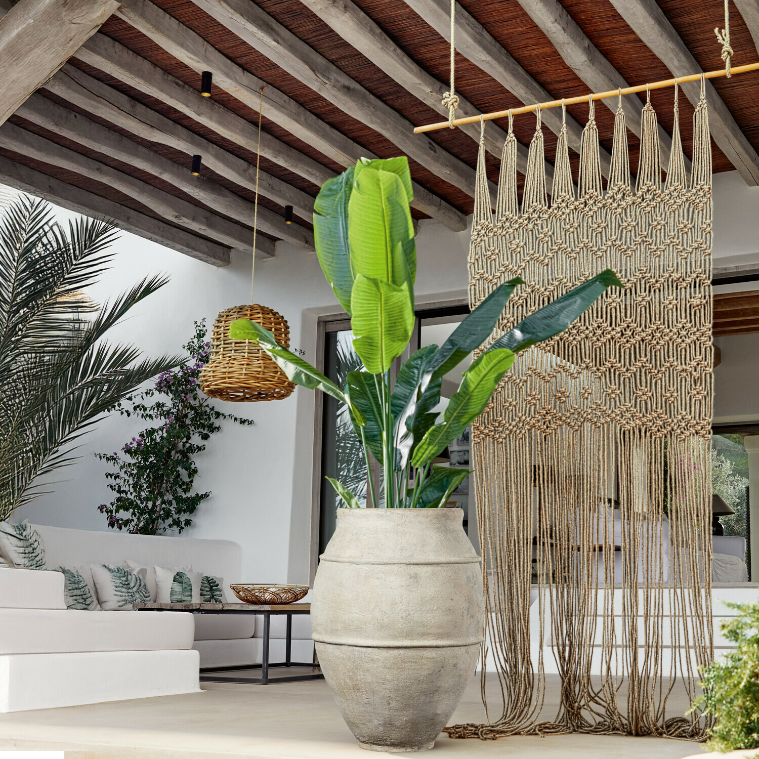 Grote lichte stenen pot met groene plant in moderne woonkamer met macramé en rotan lamp