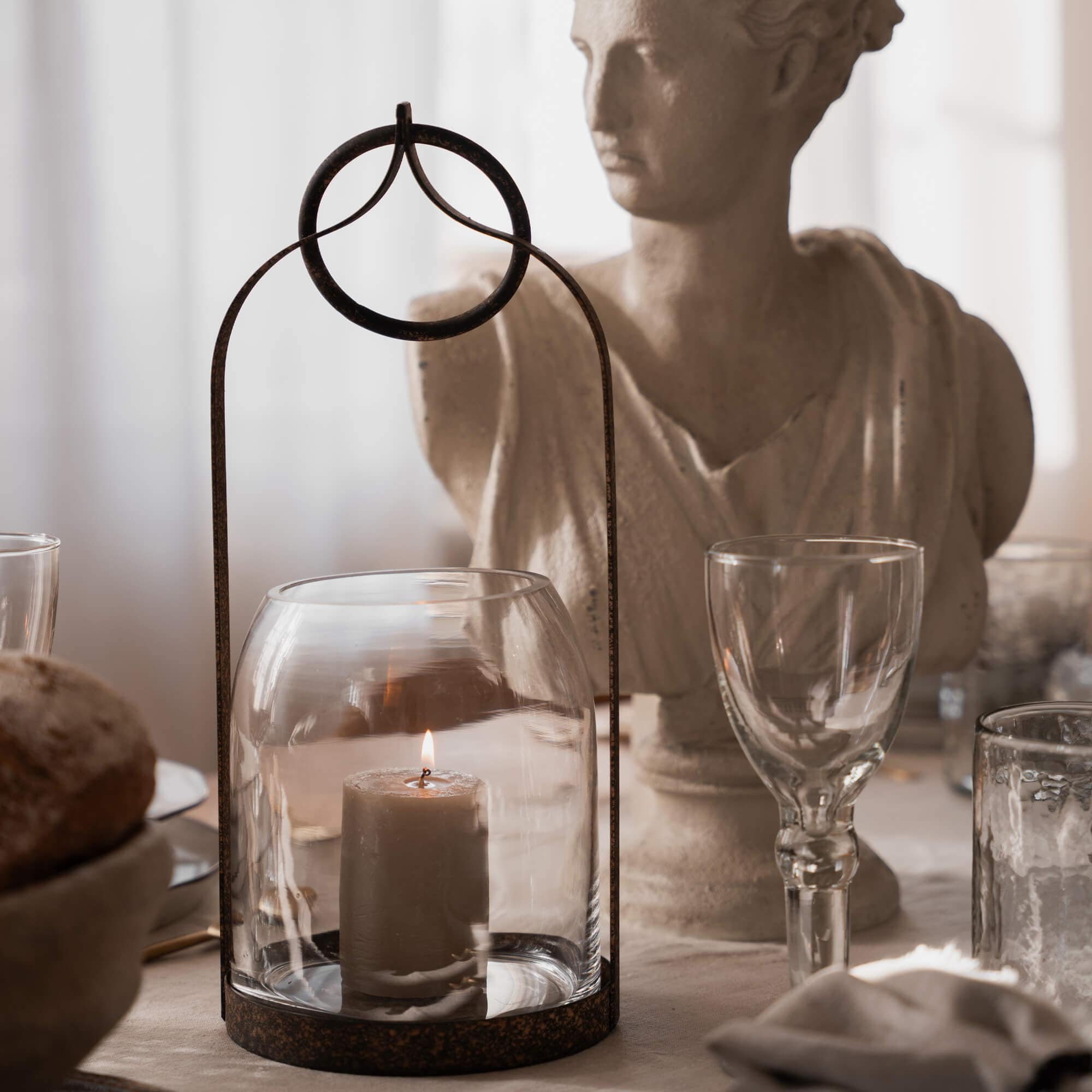 Glazen lantaarn met roestige metalen lijst en brandende kaars op rustieke tafel met decoratief beeld