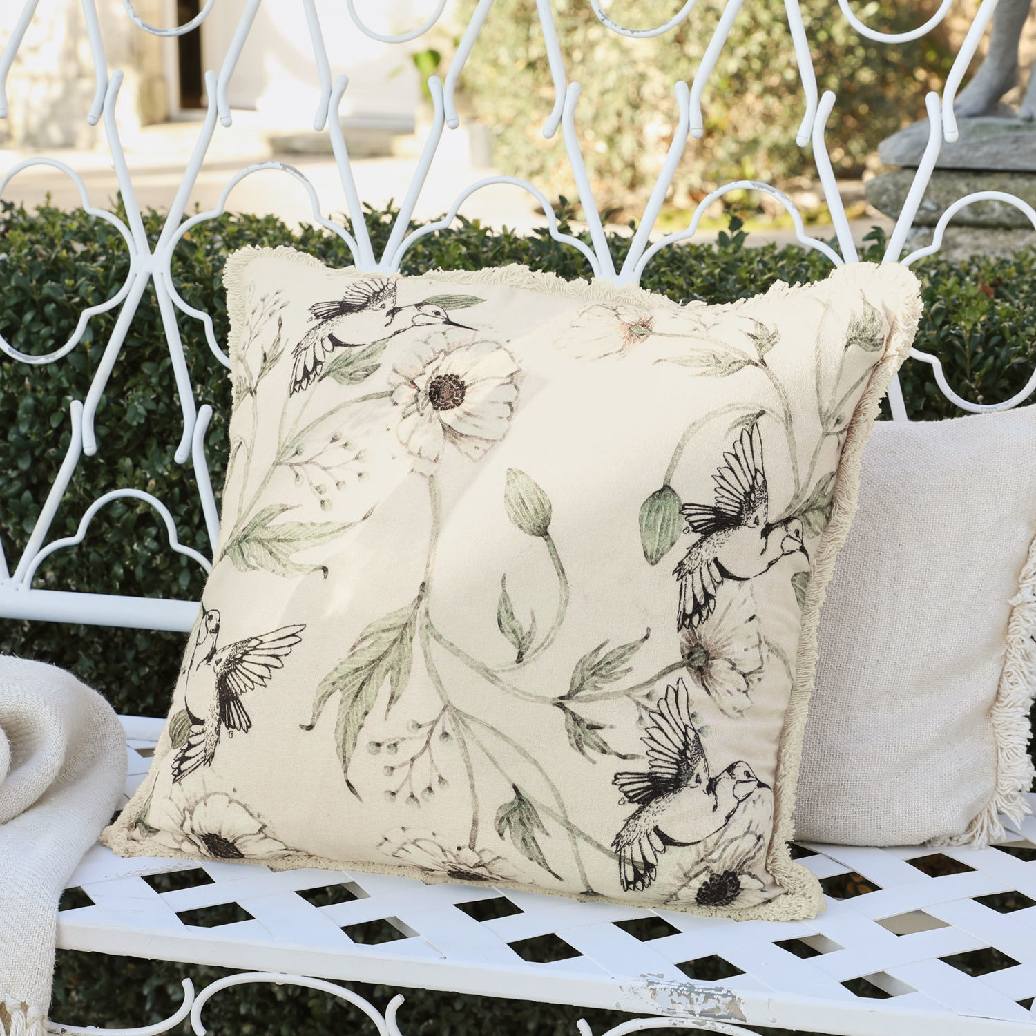 Beige sierkussen met vogel- en bloemenprint op witte metalen bank in de tuin