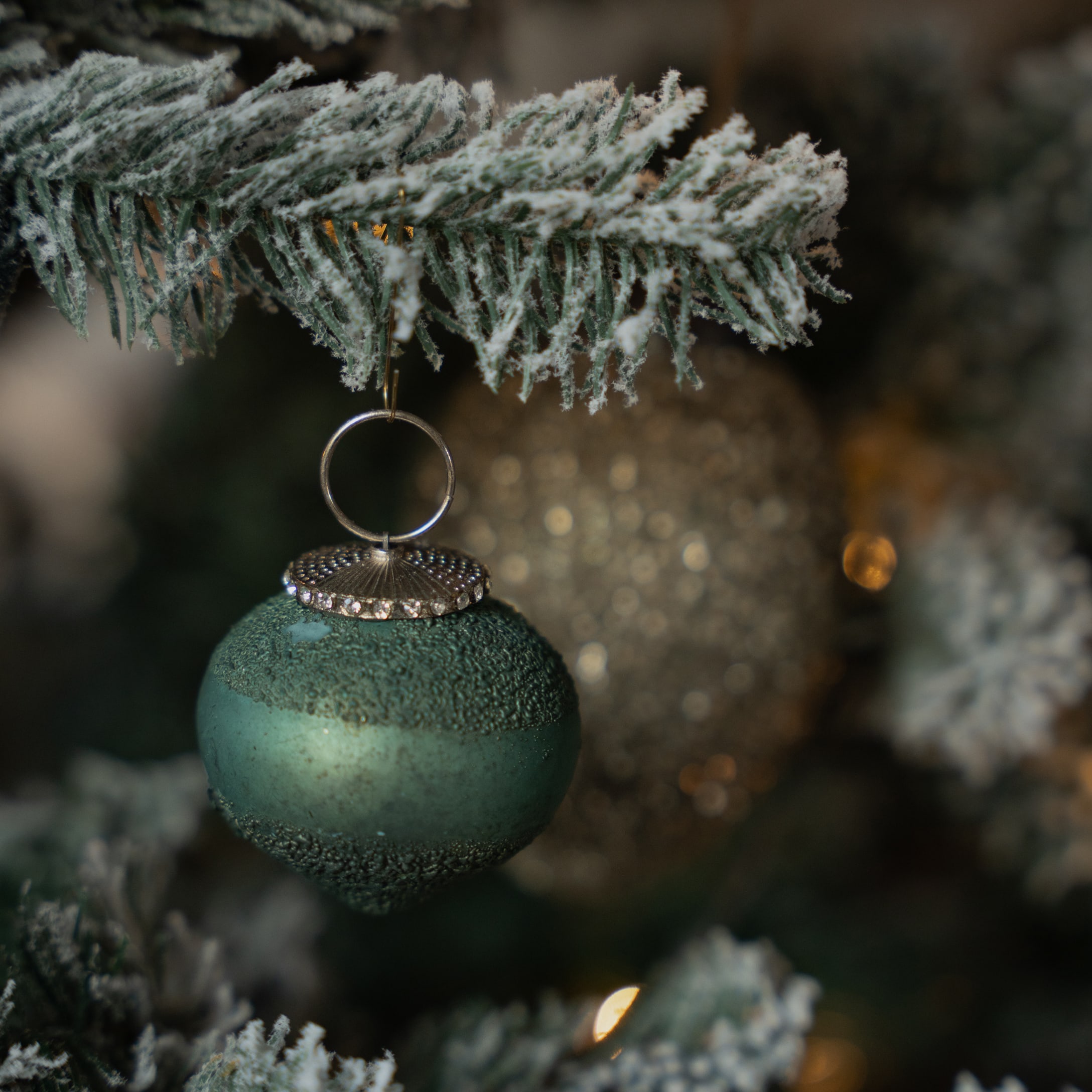 Mat groene kerstbal met textuur en zilveren haak aan besneeuwde kersttak