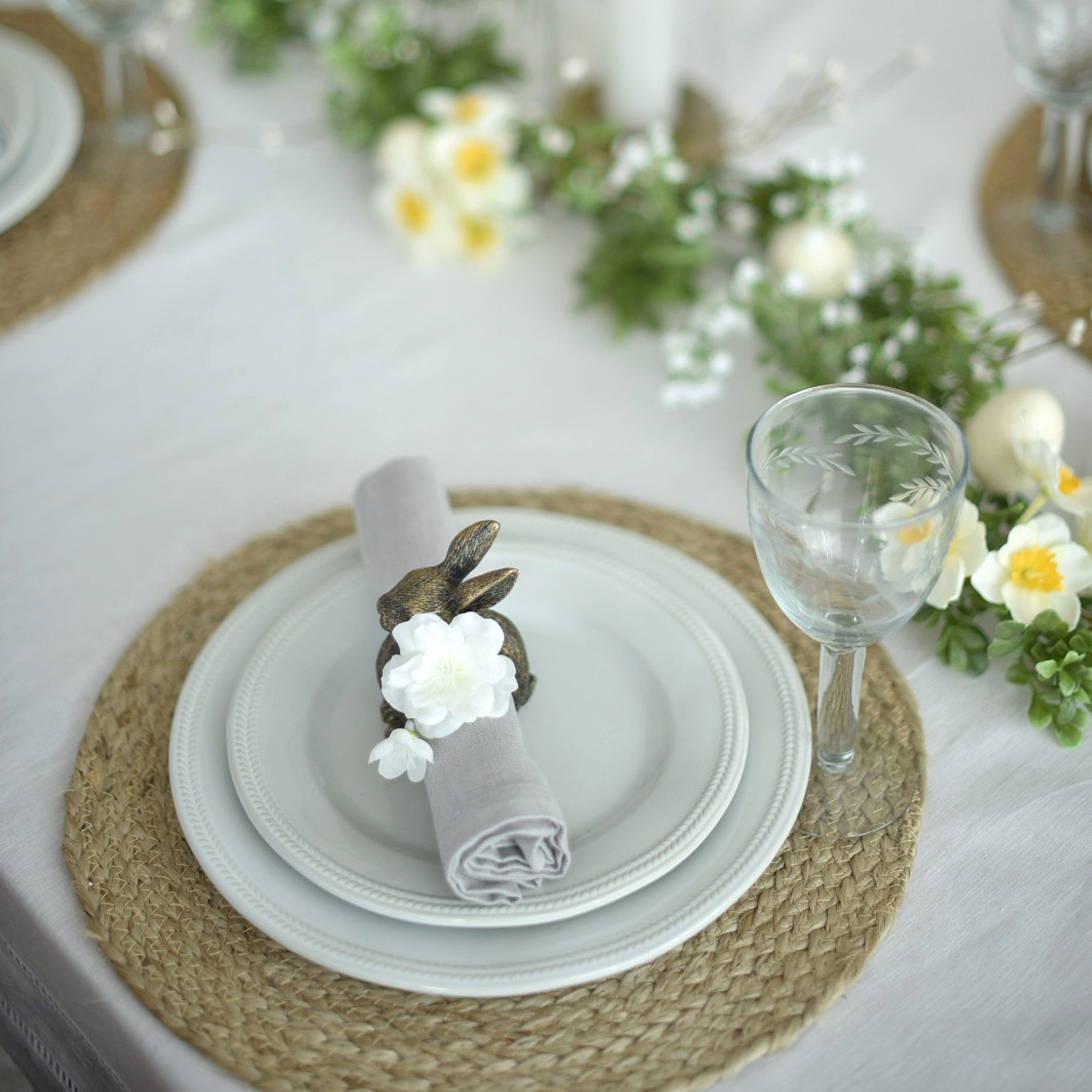 Witte borden op gevlochten placemat met konijnen servetring en fijne bloemendecoratie
