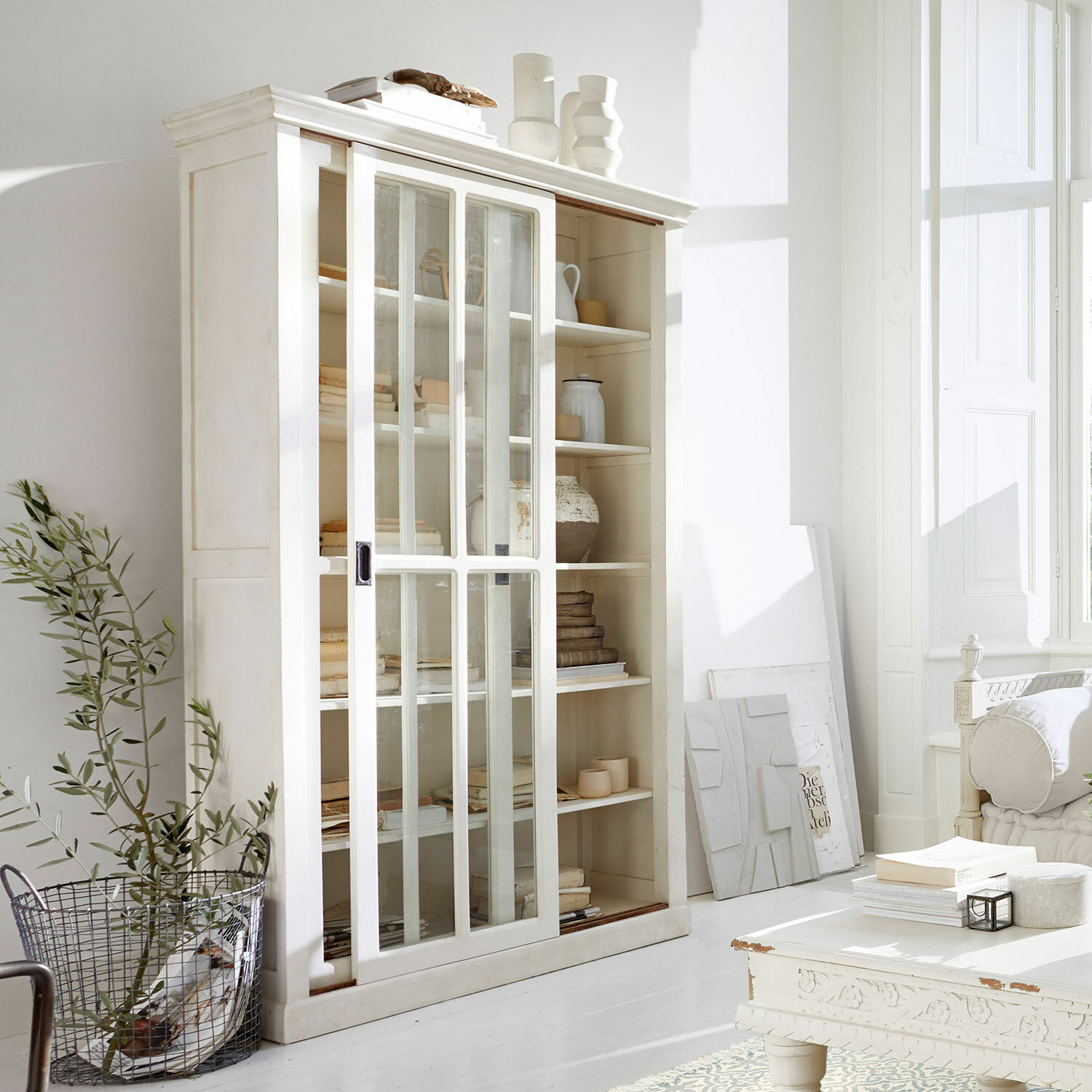 Kast Brouns Witte houten vitrinekast met glazen schuifdeuren in lichte, moderne woonkamer
