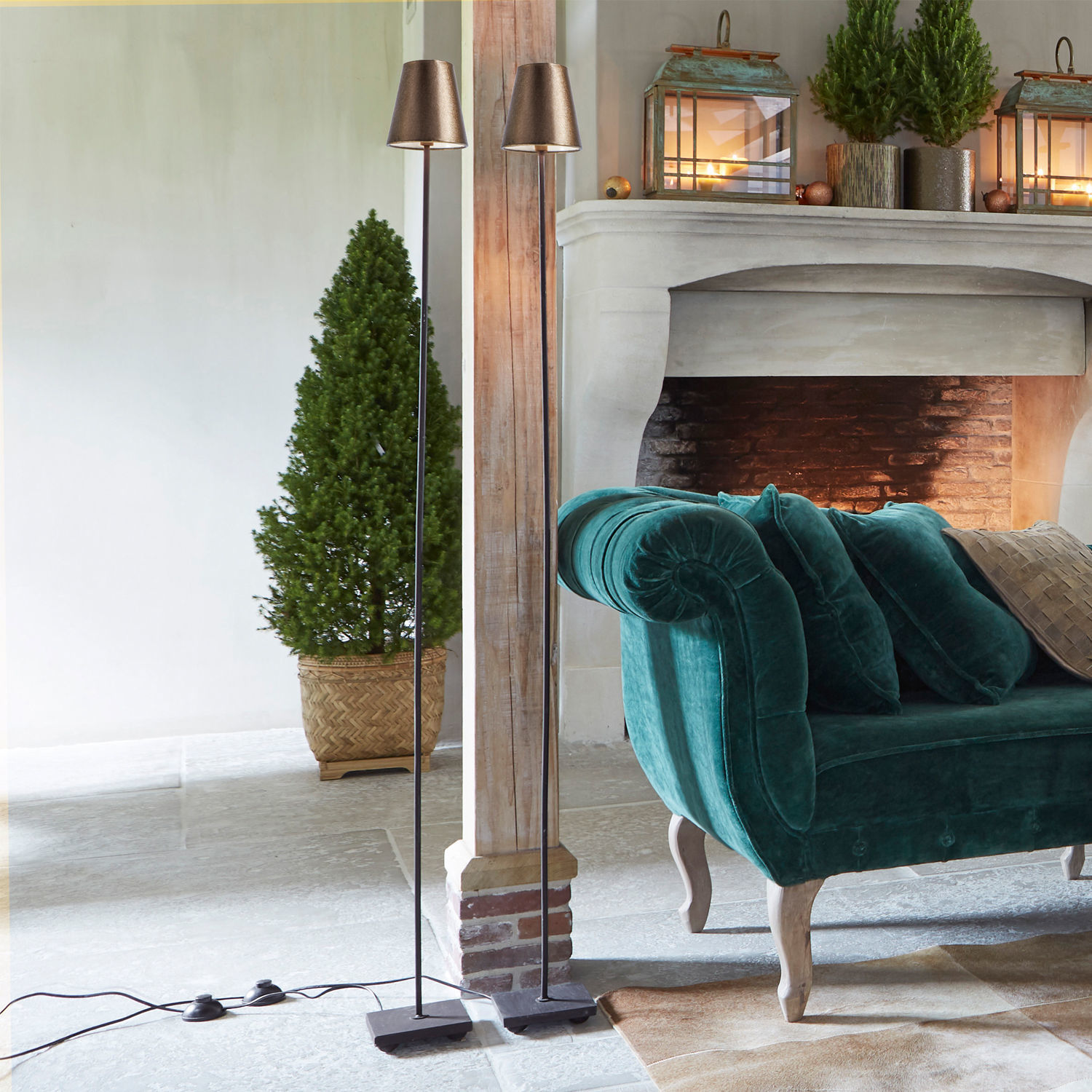 Twee zwarte metalen vloerlampen met koperen kappen in moderne woonkamer met groene fluwelen bank