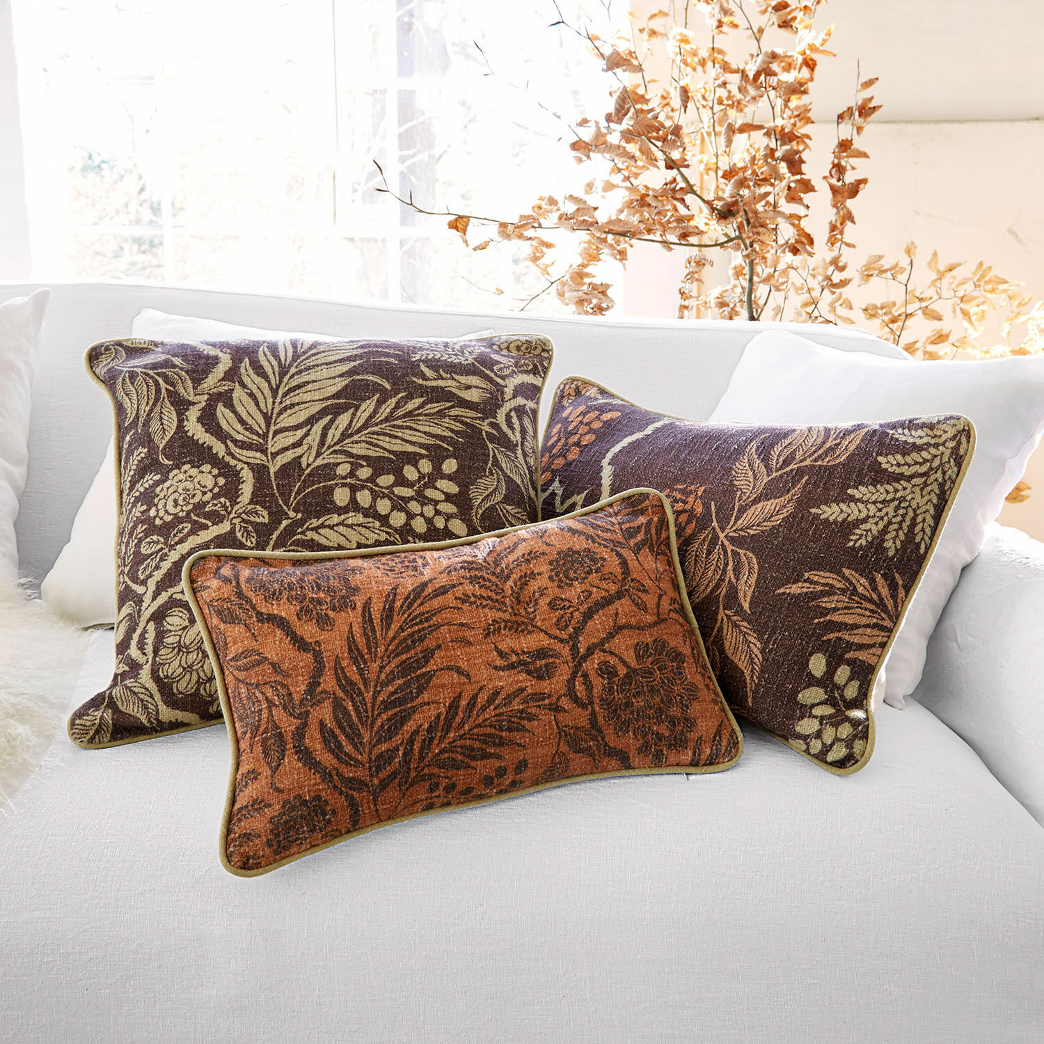 Set van drie decoratieve kussens met bladmotief in bruine en oranje tinten op een witte bank