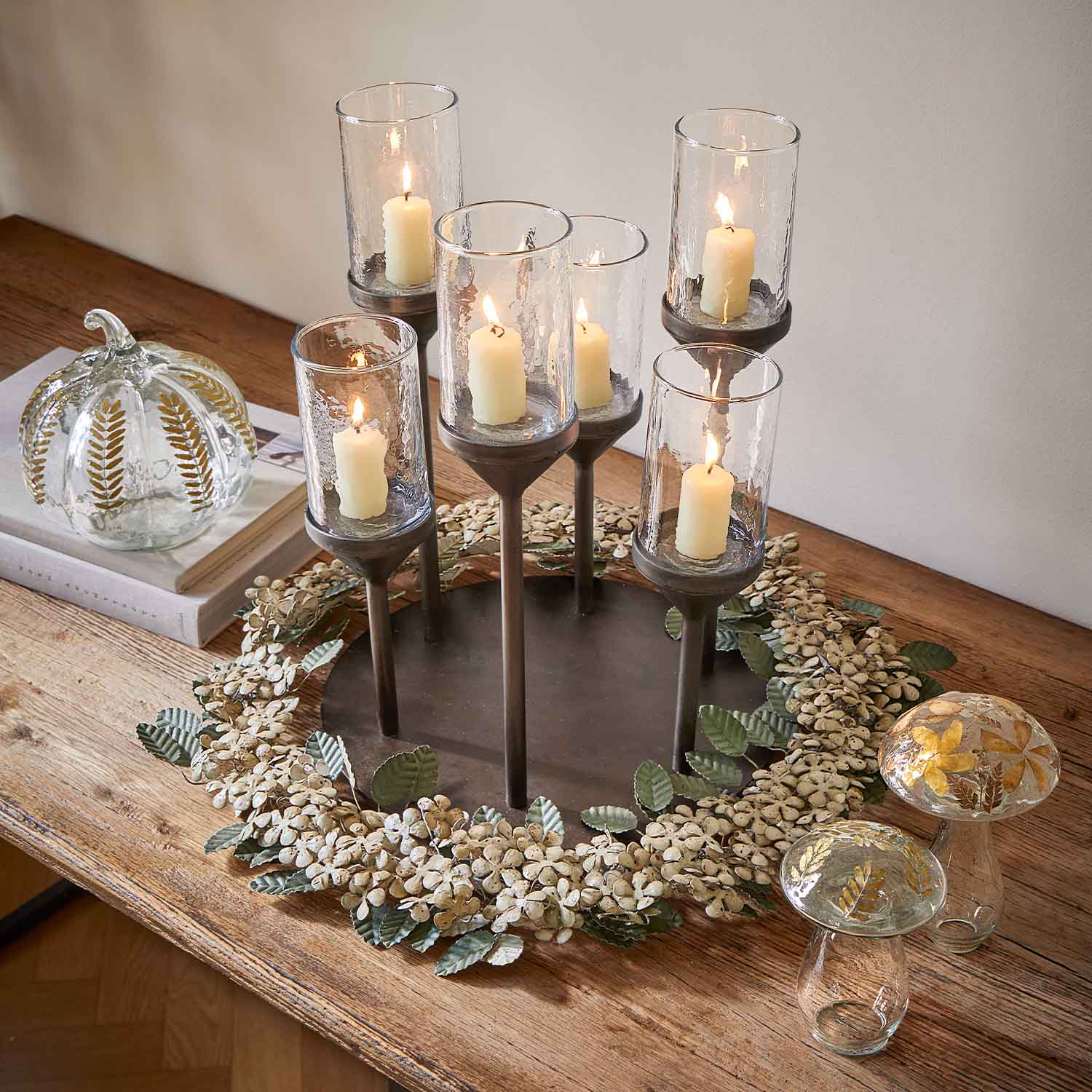 Metalen kandelaar met zes witte kaarsen in glazen houders op houten tafel met decoratieve krans
