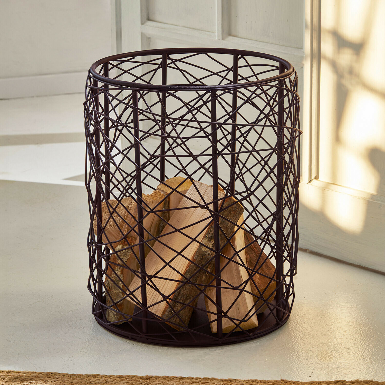 Ronde houtmand van donker metalen gaas voor het opbergen van haardhout binnenshuis