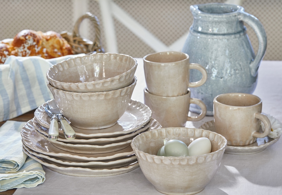 Beige keramiek servies met borden, kommen en mokken op rustieke tafel